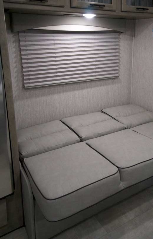 RV rental interior featuring a gray modular sofa/bed, window blinds, overhead cabinets, and light.. Coachmen Freelander 26DS 2020