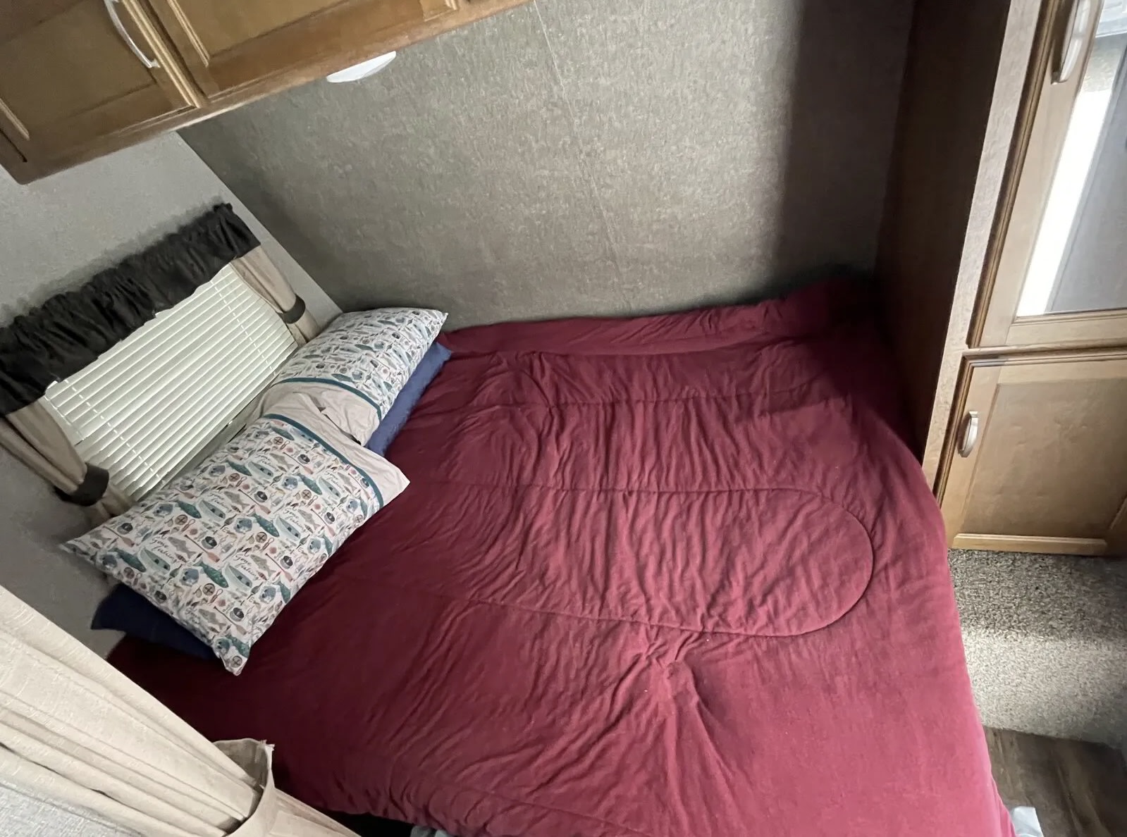 Inside an RV rental: a compact bedroom with a burgundy bed, patterned pillows, and window blinds.. Keystone Springdale 201RD 2017