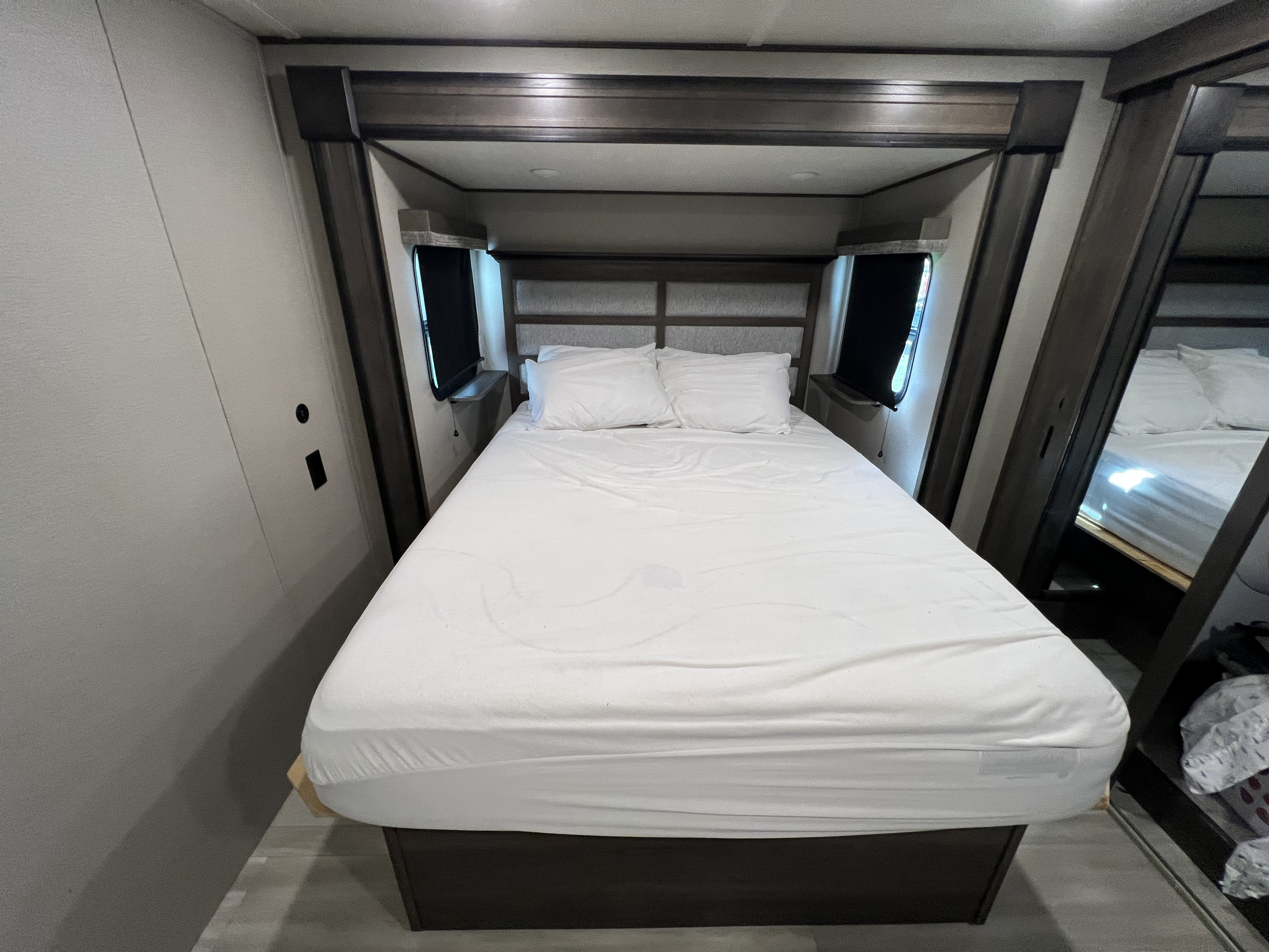 RV rental bedroom with a tidy bed, white linens, and built-in framing around windows, offering a cozy travel space.. Grand Design Solitude S-Class 2022