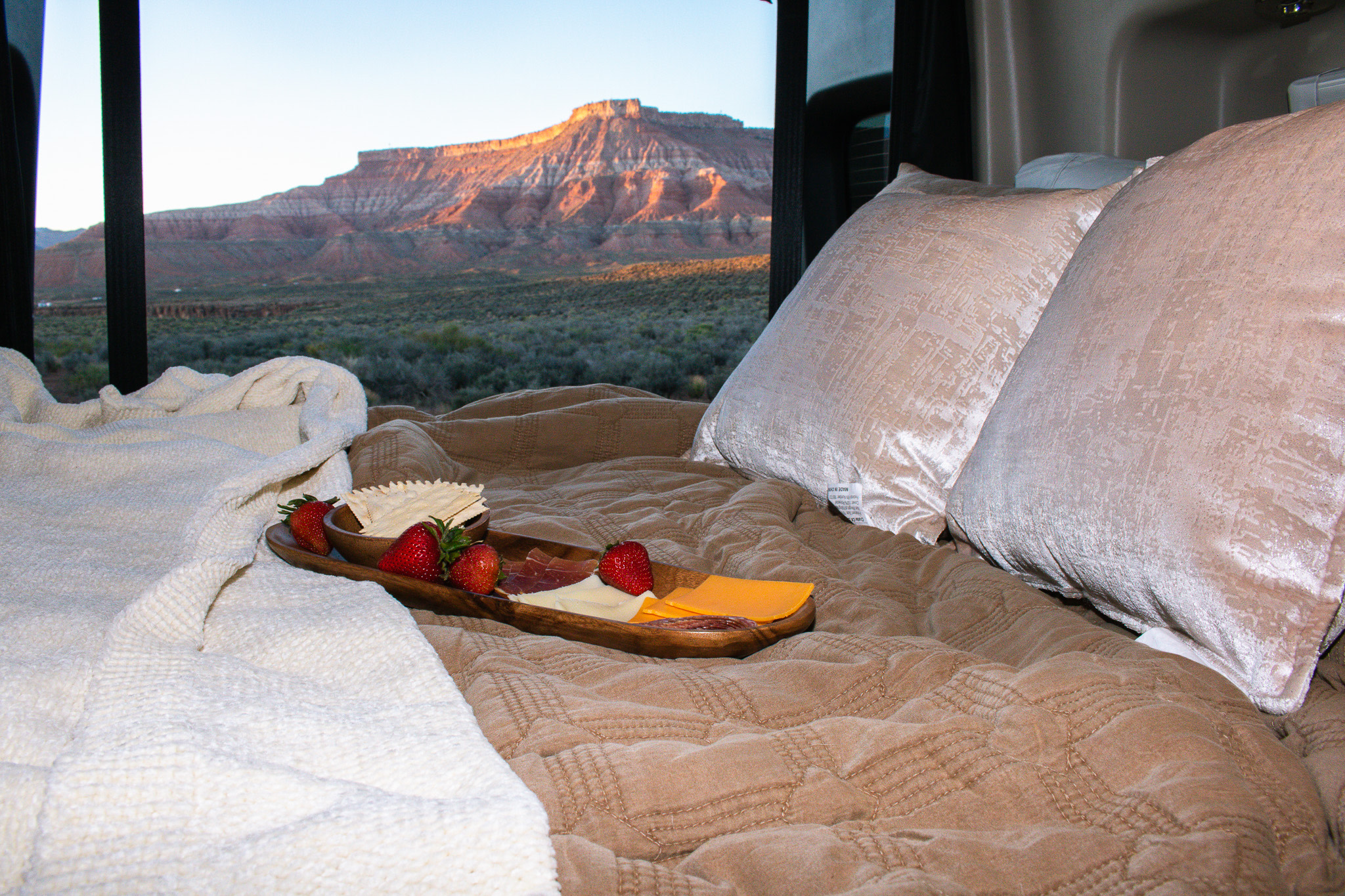 RV rental glamping: Cozy bed with charcuterie board, overlooking stunning red rock mountains at sunrise.. Entegra Coach Launch 2024