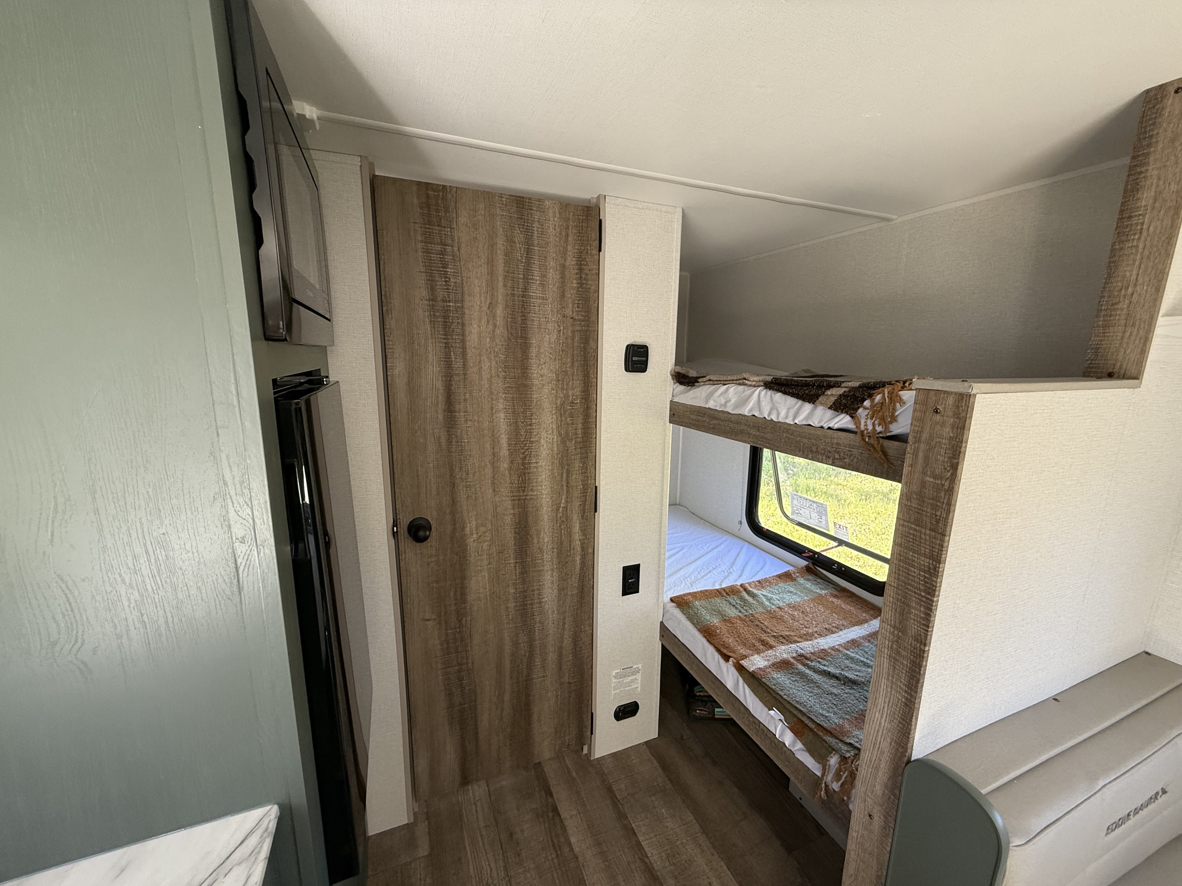 RV rental interior showing a living area with a TV, a door, and bunk beds with blankets by a window.. Heartland Eddie Bauer 17BC-H 2025