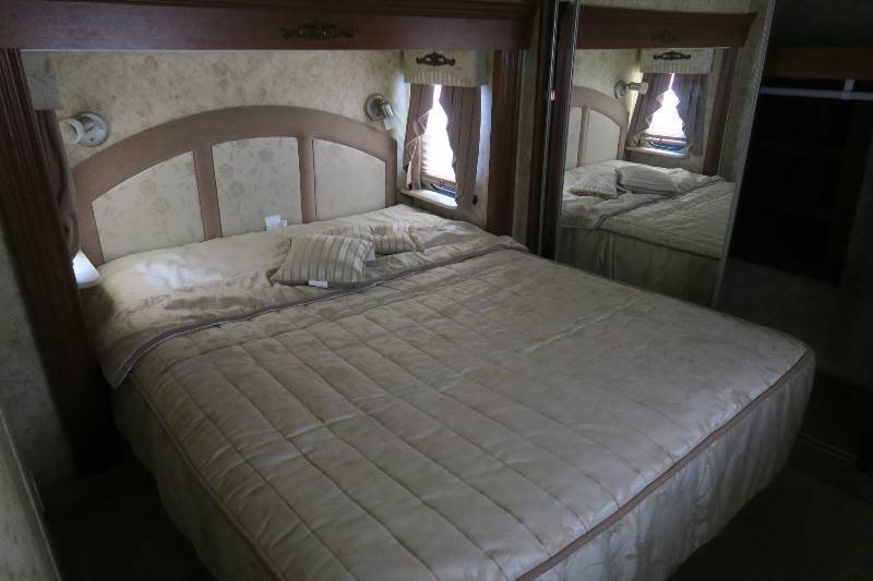 RV rental bedroom: large bed with padded headboard, side sconces, window, and mirrored closet, offering comfort.. Pilgrim International Inc Open Road 2008