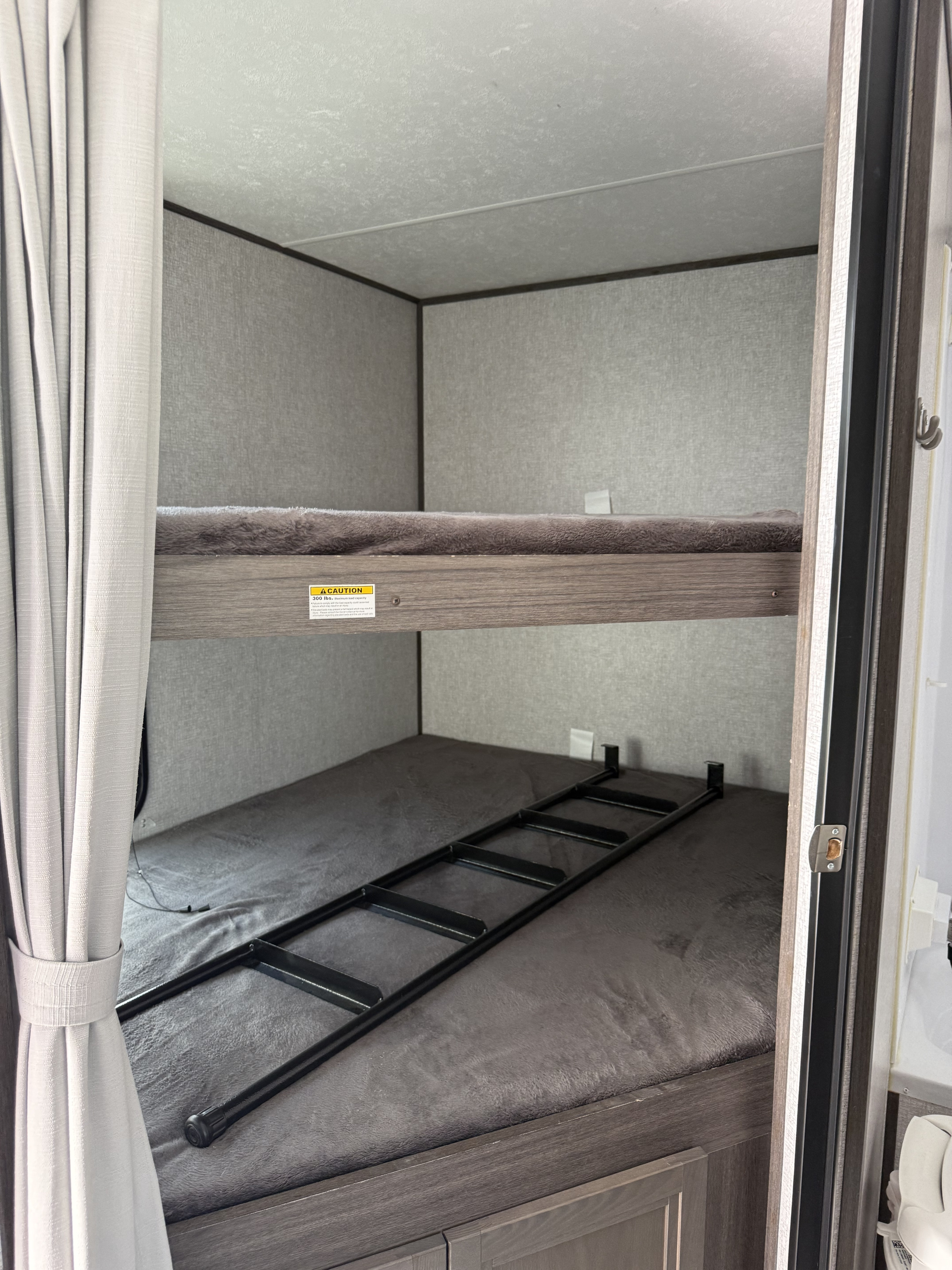 RV rental bunk beds: A cozy sleeping area with two beds, a ladder for access, and light grey privacy curtains.. Dutchmen Kodiak Ultra Lite 2021