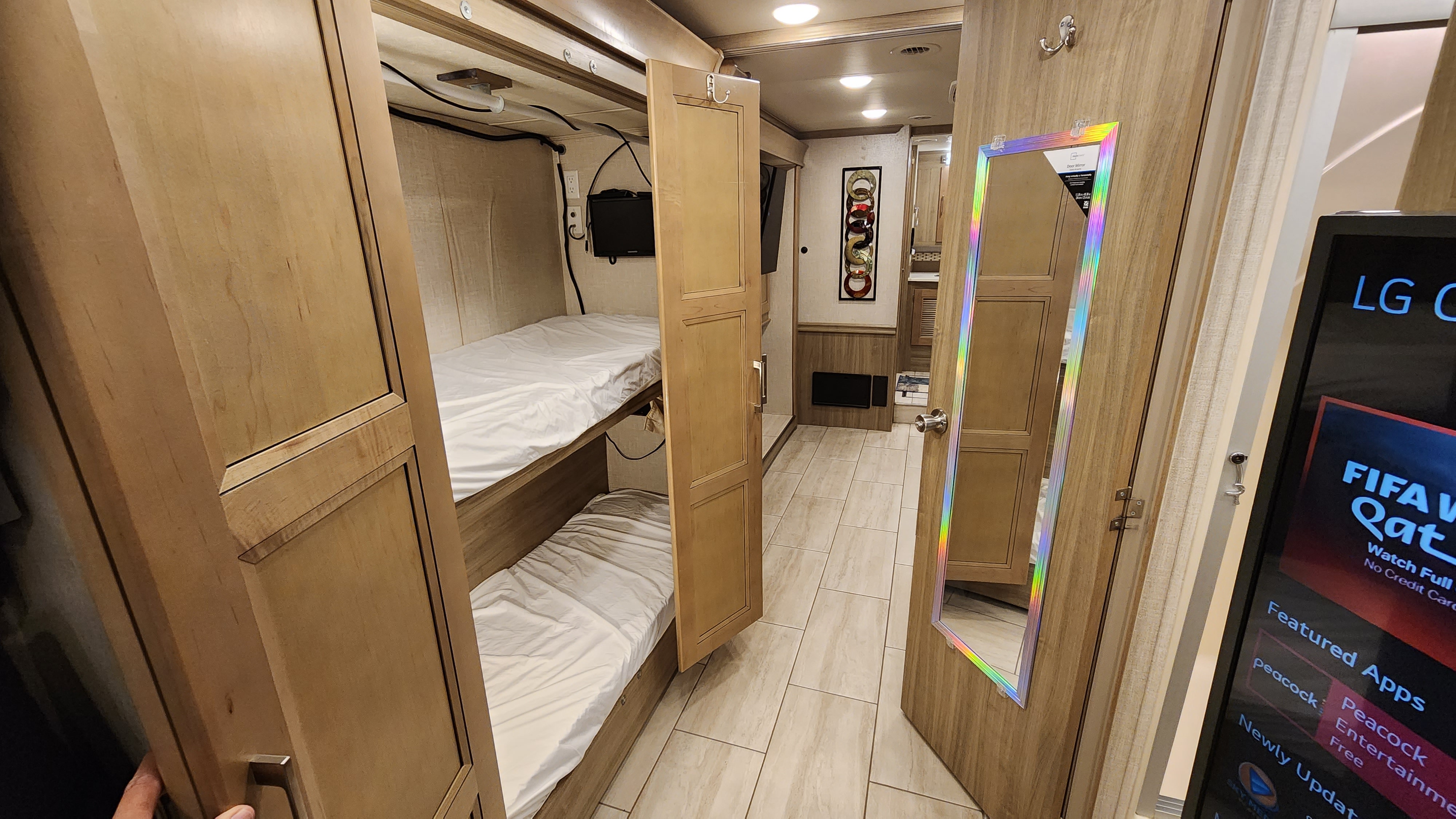 This RV rental interior features bunk beds with white sheets, wooden cabinetry, a mirror door, and a large entertainment screen.. Forest River Coachmen Sportscoach 2019