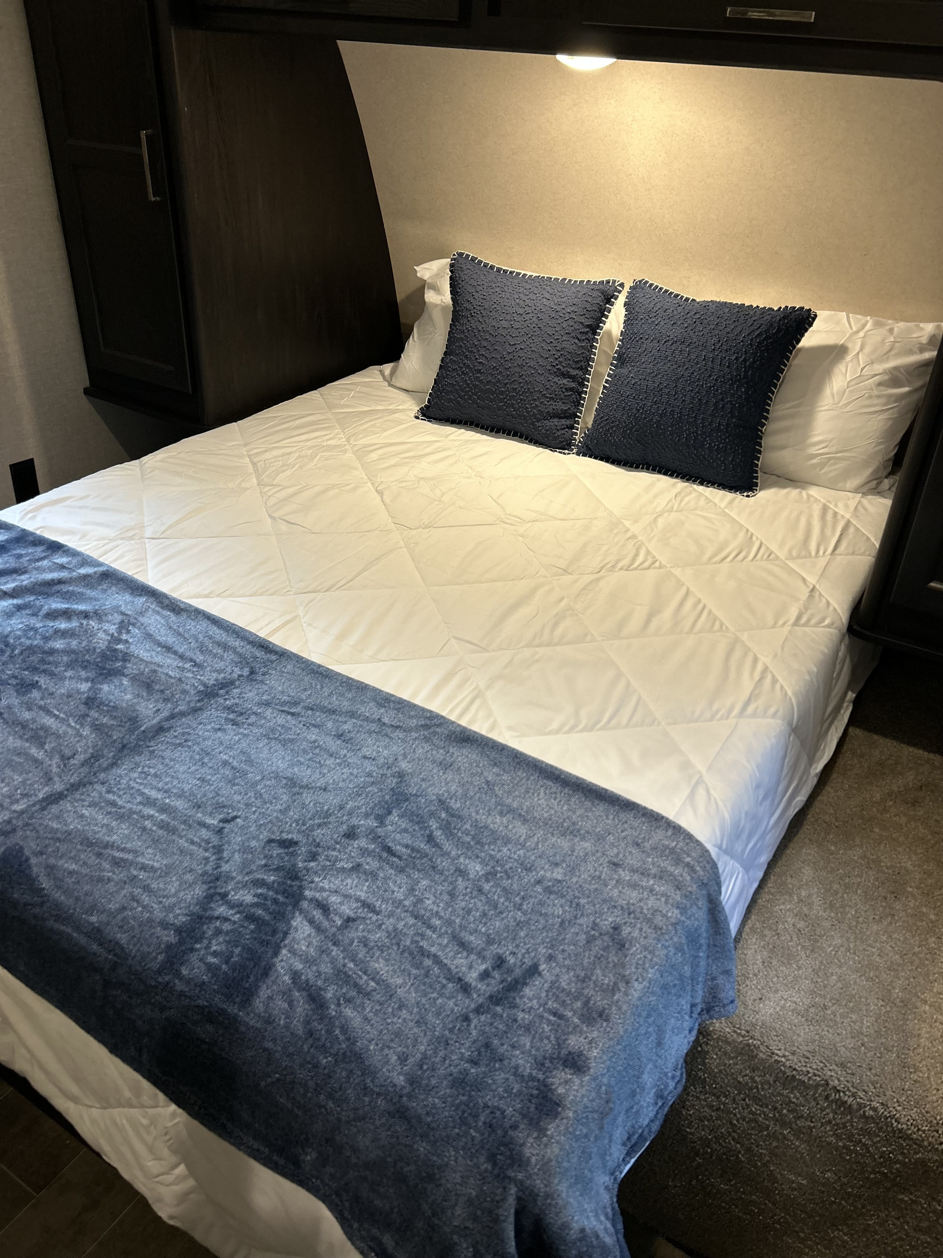 Clean and comfortable RV rental bedroom features white bedding, blue pillows, and dark wood storage.. Keystone Impact 2018