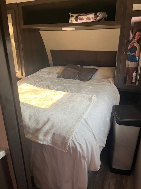 RV rental bedroom: a made bed with white linens, overhead storage, and a mirrored closet reflecting the photographer.. Grand Design Transcend Xplor 2023