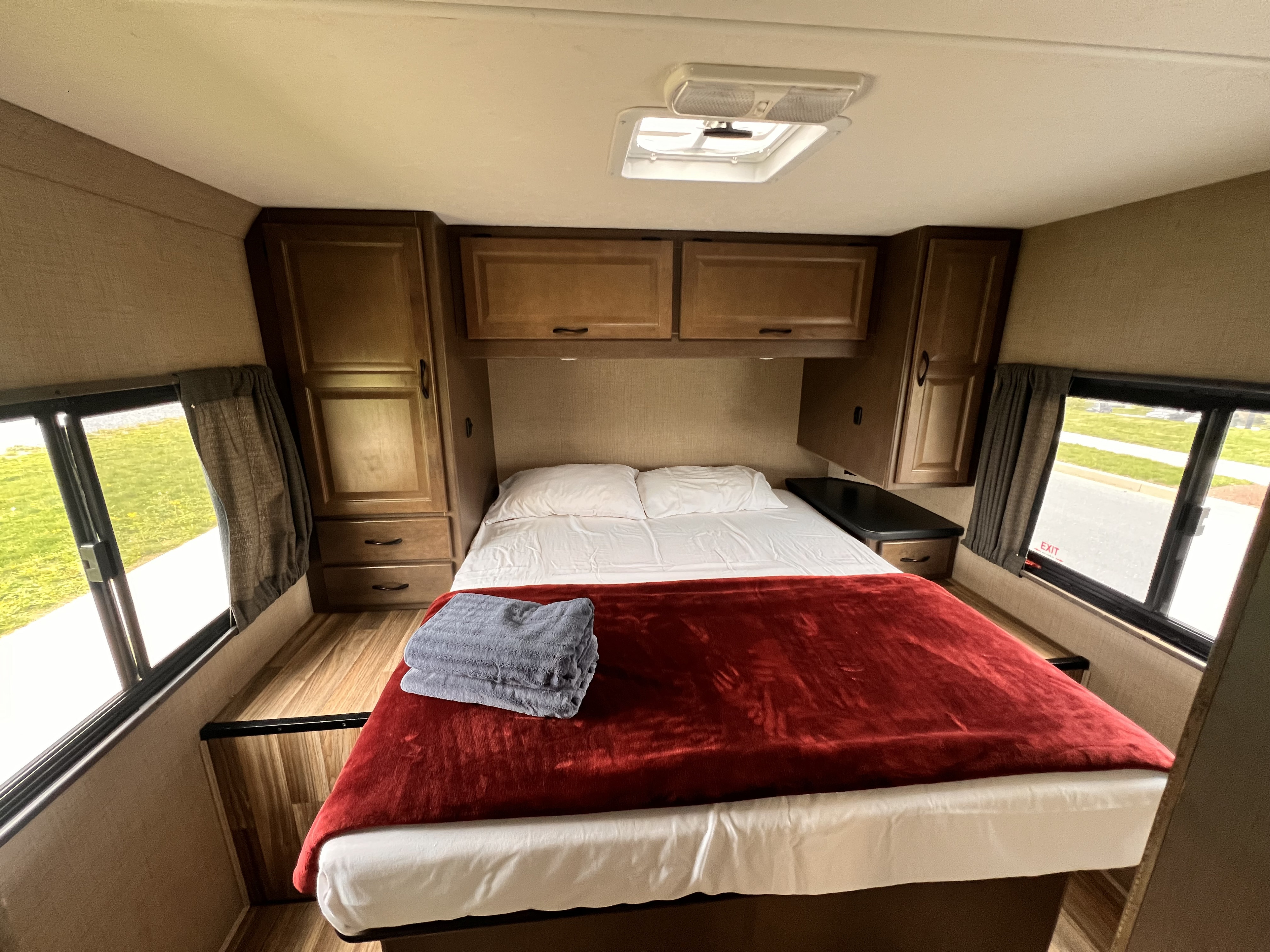 Cozy RV rental bedroom with comfortable bed, wooden cabinetry, and windows on both sides. Ideal travel lodging.. Thor Majestic 2019
