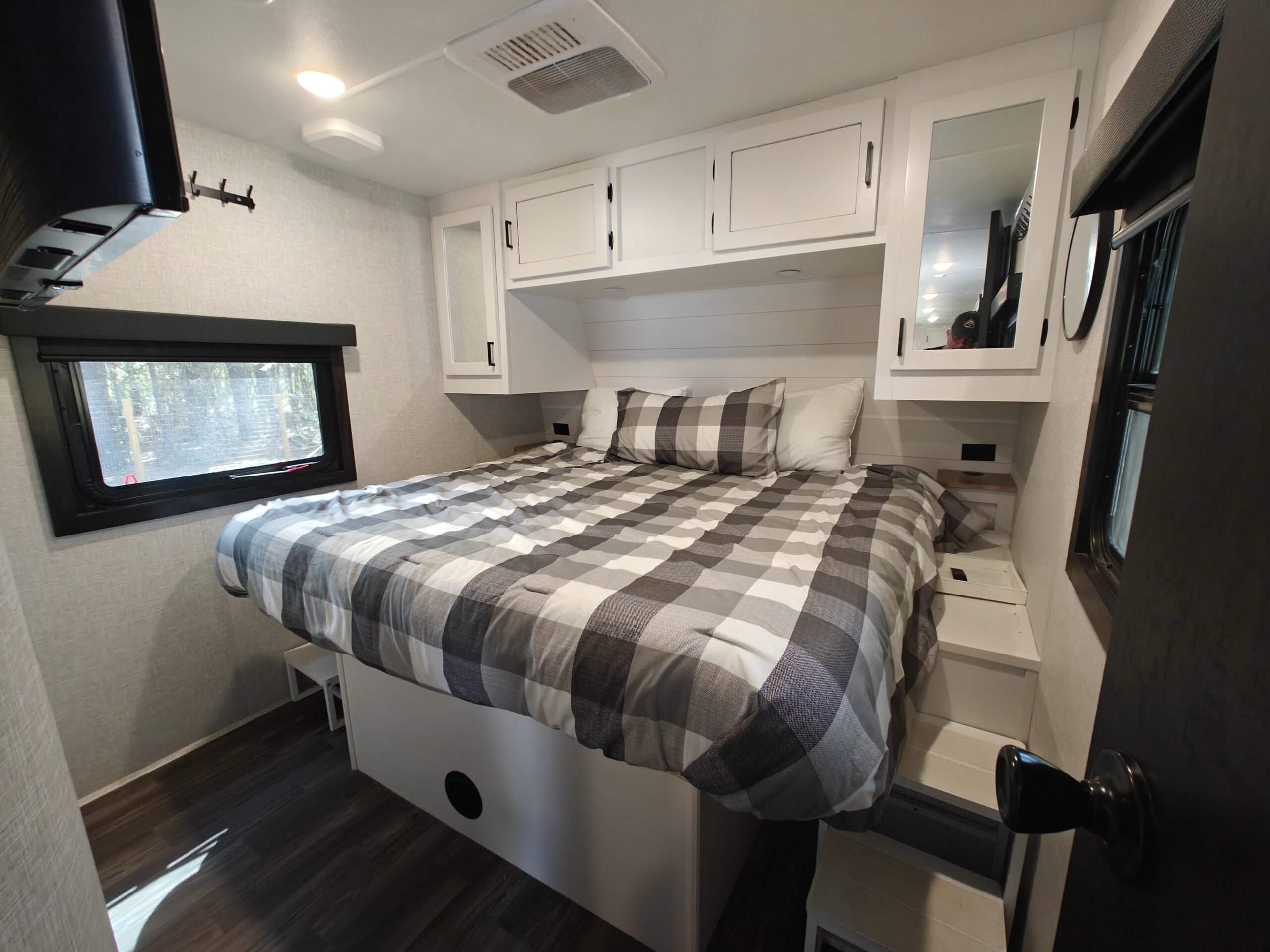 This RV rental bedroom features a cozy plaid bed, modern white cabinets, and a window view. Perfect for your next adventure!. Highland Ridge Open Range Light 2024