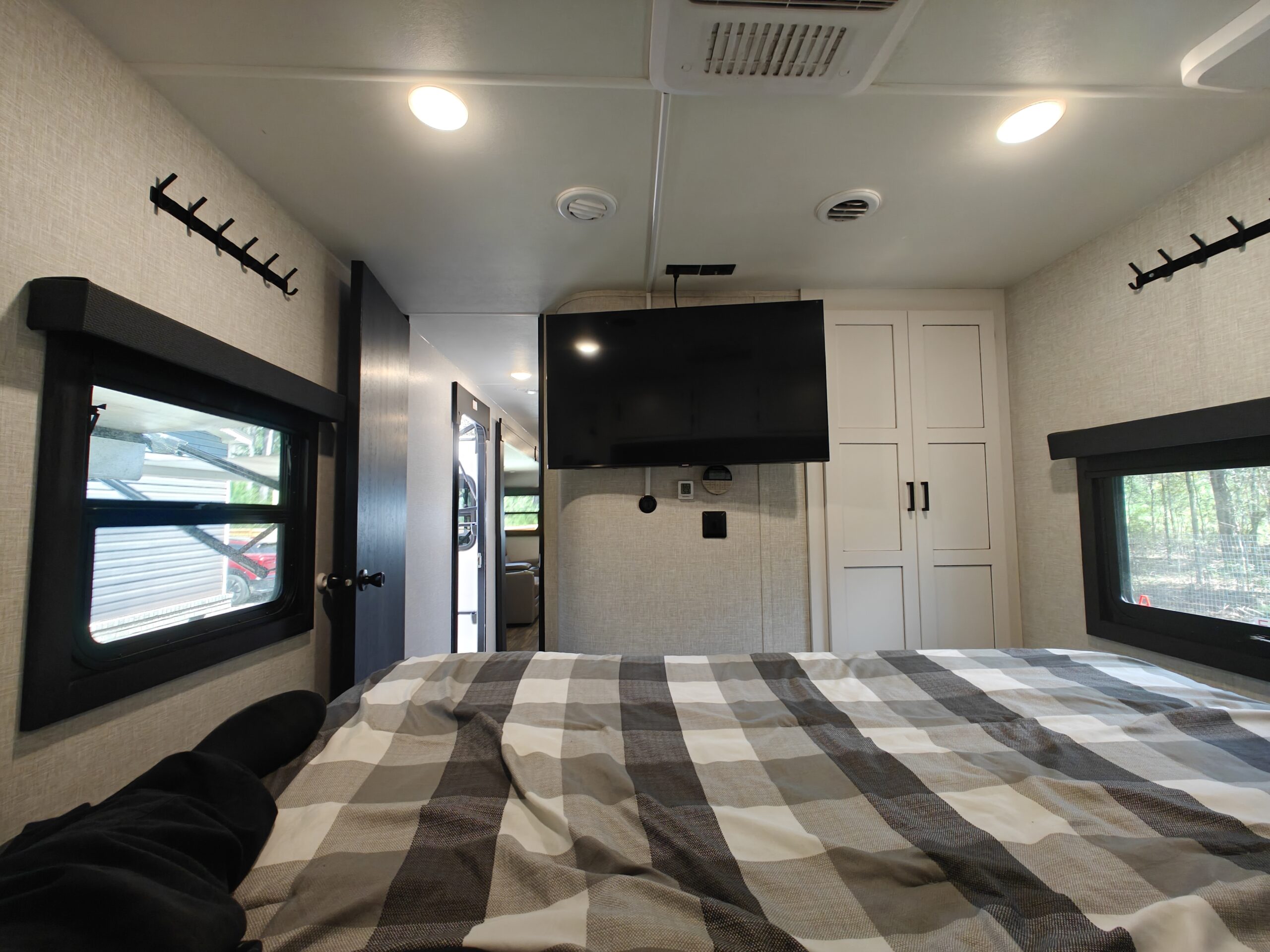 Cozy RV rental bedroom with TV, plaid bed, and windows. Ideal for travel.. Highland Ridge Open Range Light 2024