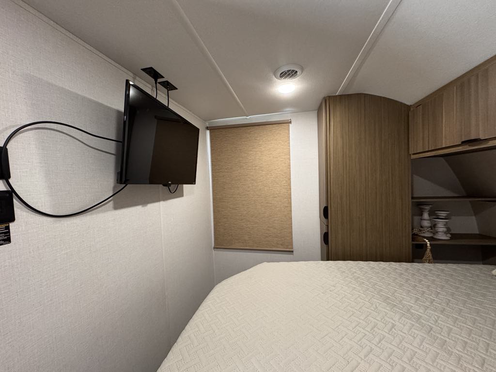 RV rental bedroom interior: shows a cozy bed, wall-mounted TV, window with shade, and wooden cabinets.. Forest River Salem 31kqbts 2025