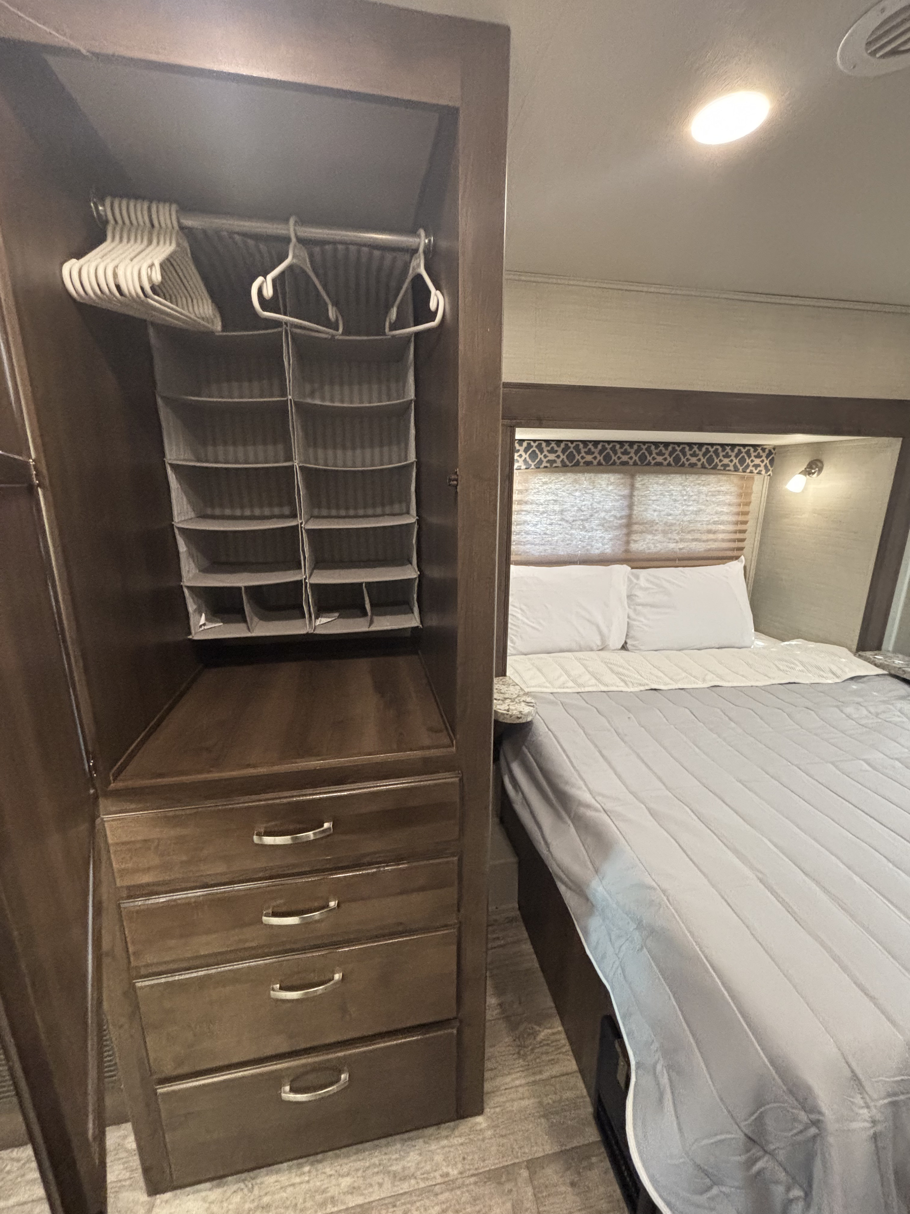 RV rental bedroom: A dark wood wardrobe with hangers and a fabric organizer stands next to a cozy bed with white pillows.. Jayco Redhawk 2018