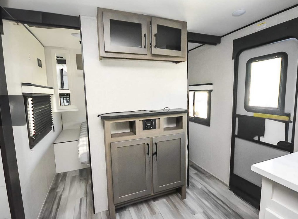 Modern RV rental interior with a living space, entertainment cabinet, and glimpse into a rear sleeping area.. Jayco Jay Flight 2024