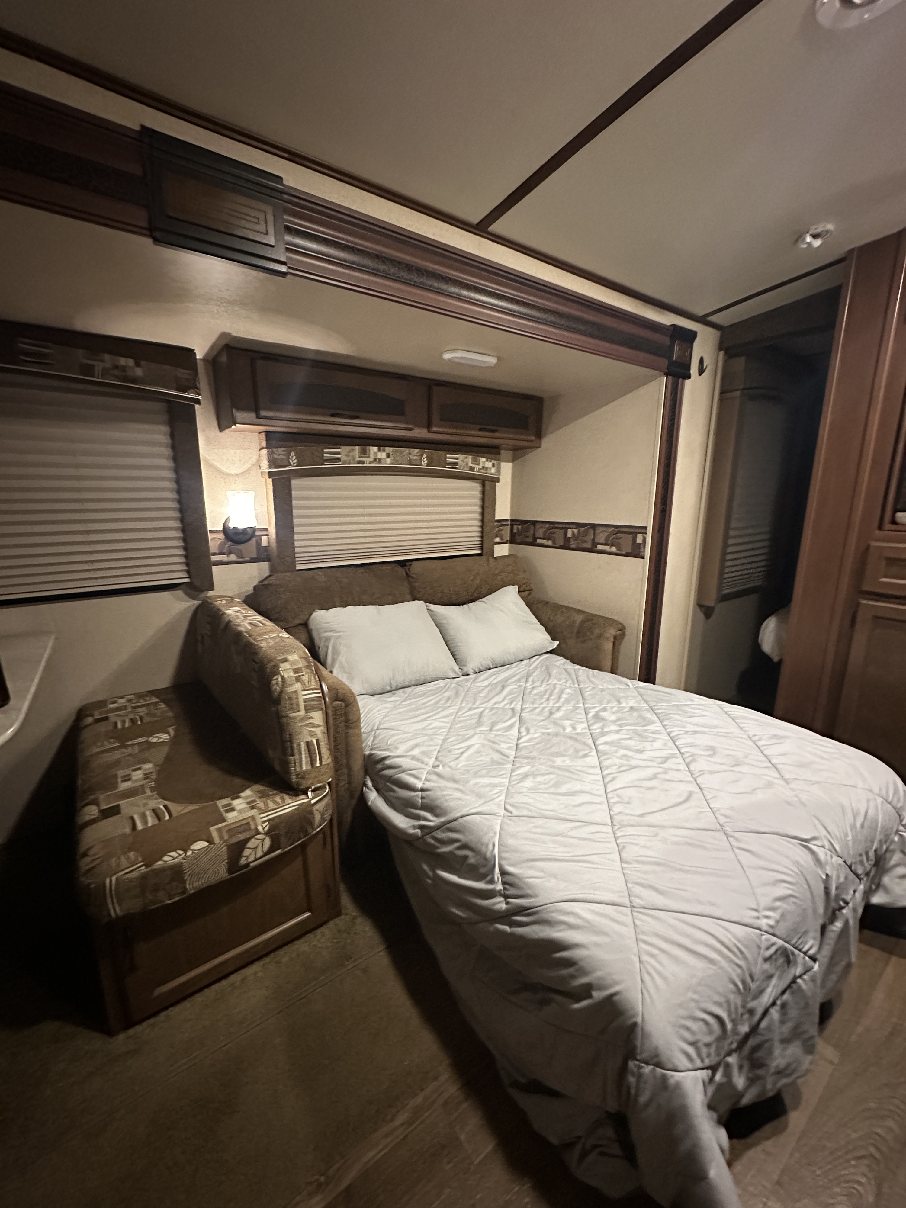 Cozy RV rental interior. A sofa bed, extended & covered by a light comforter, with dark wood cabinetry & blinds.. Jayco White Hawk Ultra Lite 2015