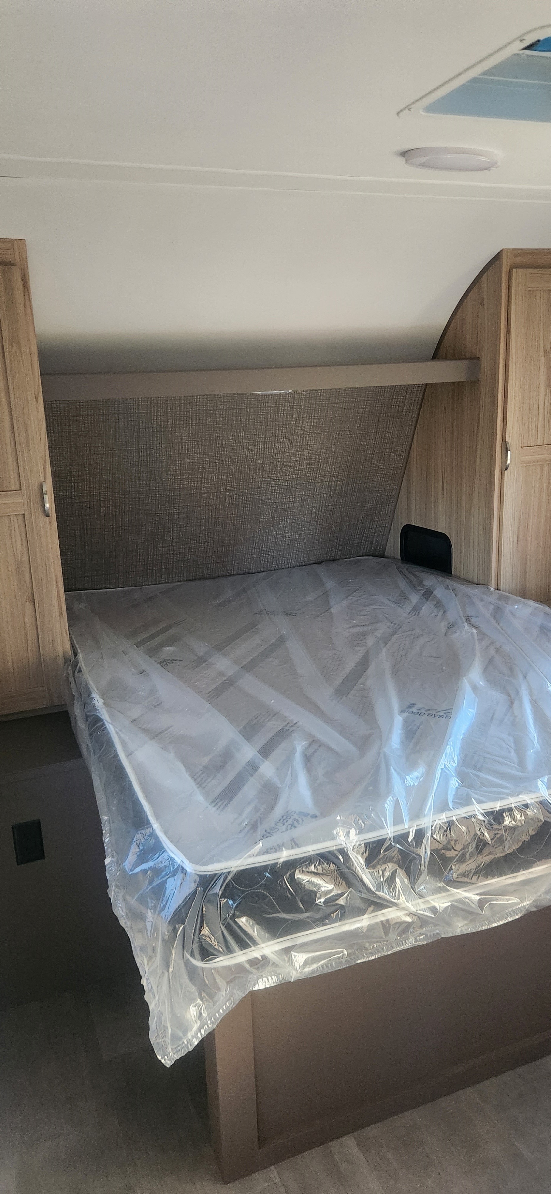 Compact RV rental bedroom, featuring a new, plastic-wrapped mattress, built-in storage, and textured headboard.. Cruiser RV Avenir 2024
