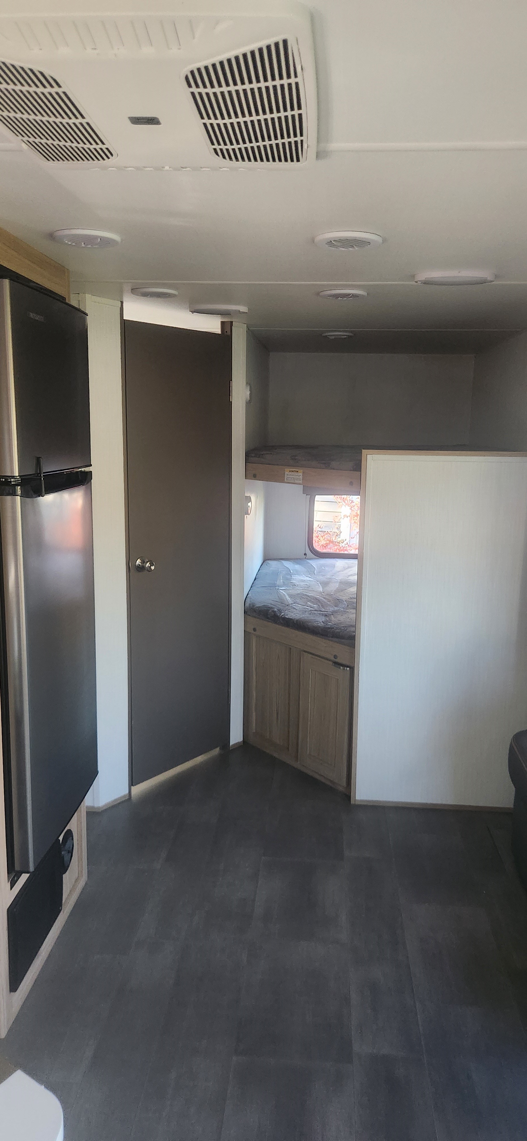 RV rental interior: fridge, private door, and two bunk beds. Features dark flooring and ceiling AC.. Cruiser RV Avenir 2024