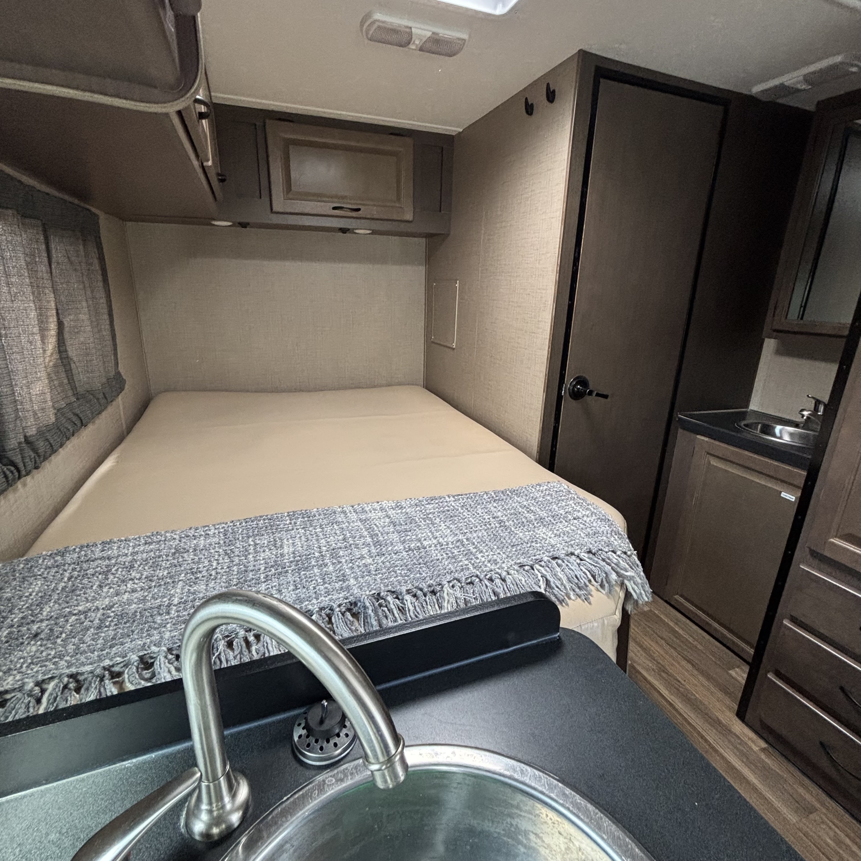 This compact RV rental interior features a comfortable bed, overhead cabinets, and a convenient kitchen sink.. Thor Majestic 2019