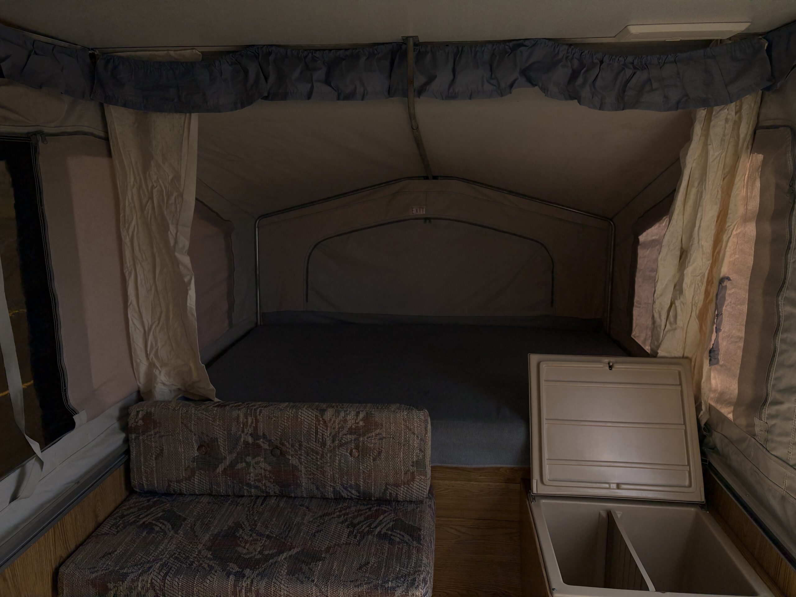 Interior of an RV rental pop-up camper with a comfy bed, couch, and cooler storage.. Forest River Palomino Colt 1994