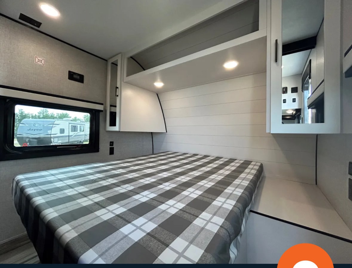 Experience comfort in this modern RV rental bedroom. Features a plaid bed, cabinets, and a window view, ideal for your next trip.. Jayco 267BHS 2025