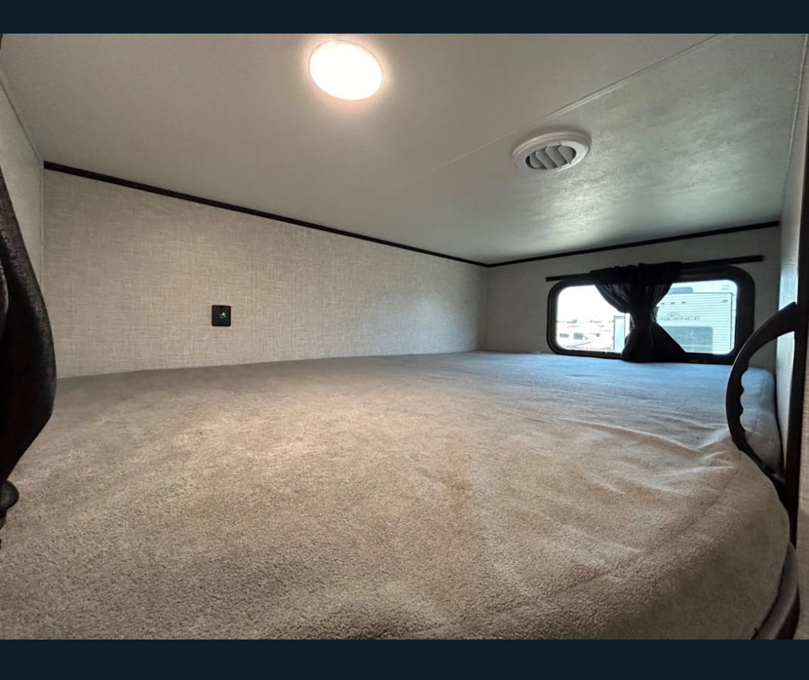 Cozy RV rental sleeping area with a comfortable carpeted bunk, window, and overhead light.. Jayco 267BHS 2025