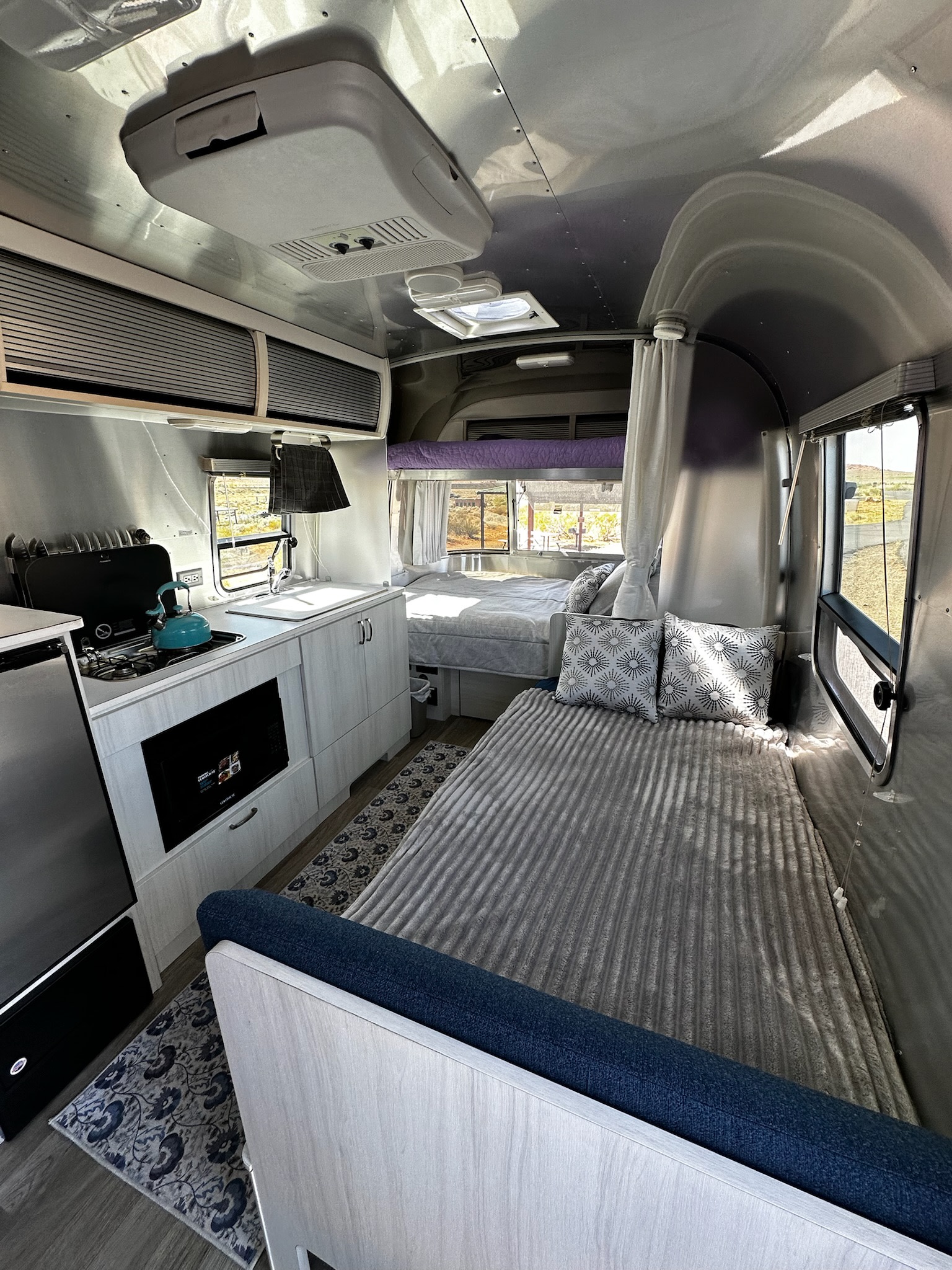 Inside a bright **RV rental** showcasing a kitchen with blue kettle, comfy sleeping areas, and light-filled windows. Ready to travel!. Airstream Bambi 2021