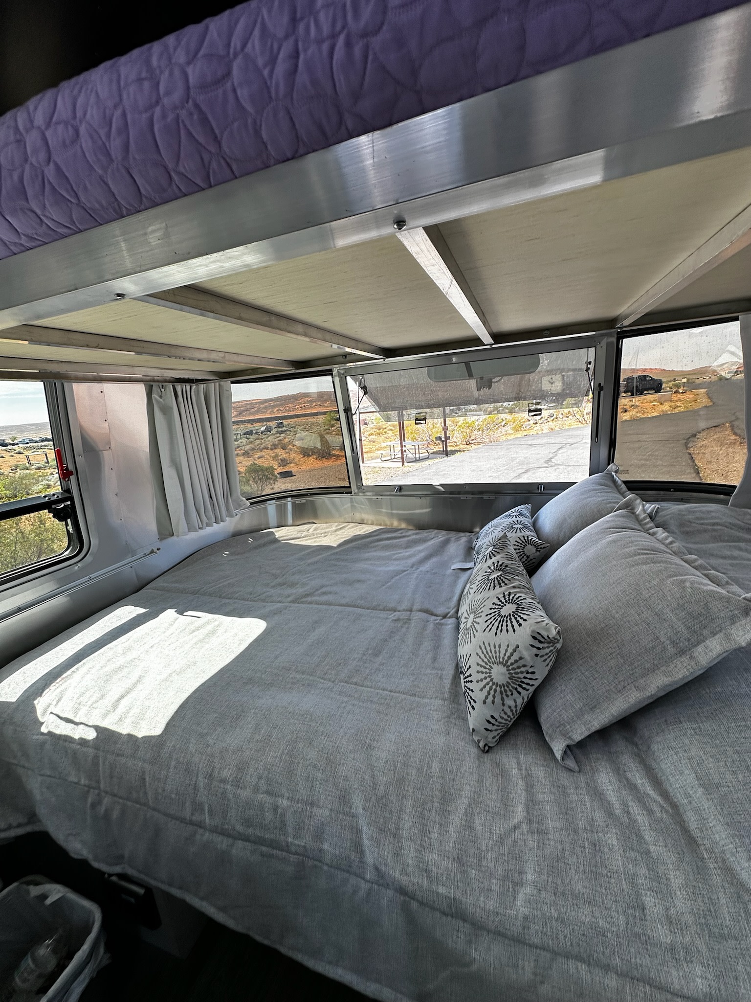 Cozy RV rental bedroom featuring a spacious bed, upper bunk, and scenic desert views through the large windows.. Airstream Bambi 2021