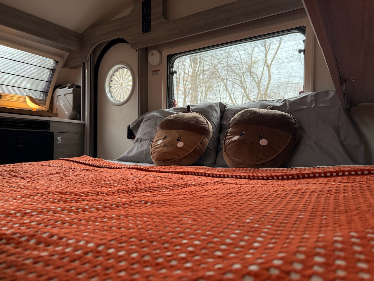 Cozy RV rental bedroom featuring a bed with acorn pillows, a bird lamp, and a nature view. Ideal for travel.. nuCamp Ultimate Toys 2023