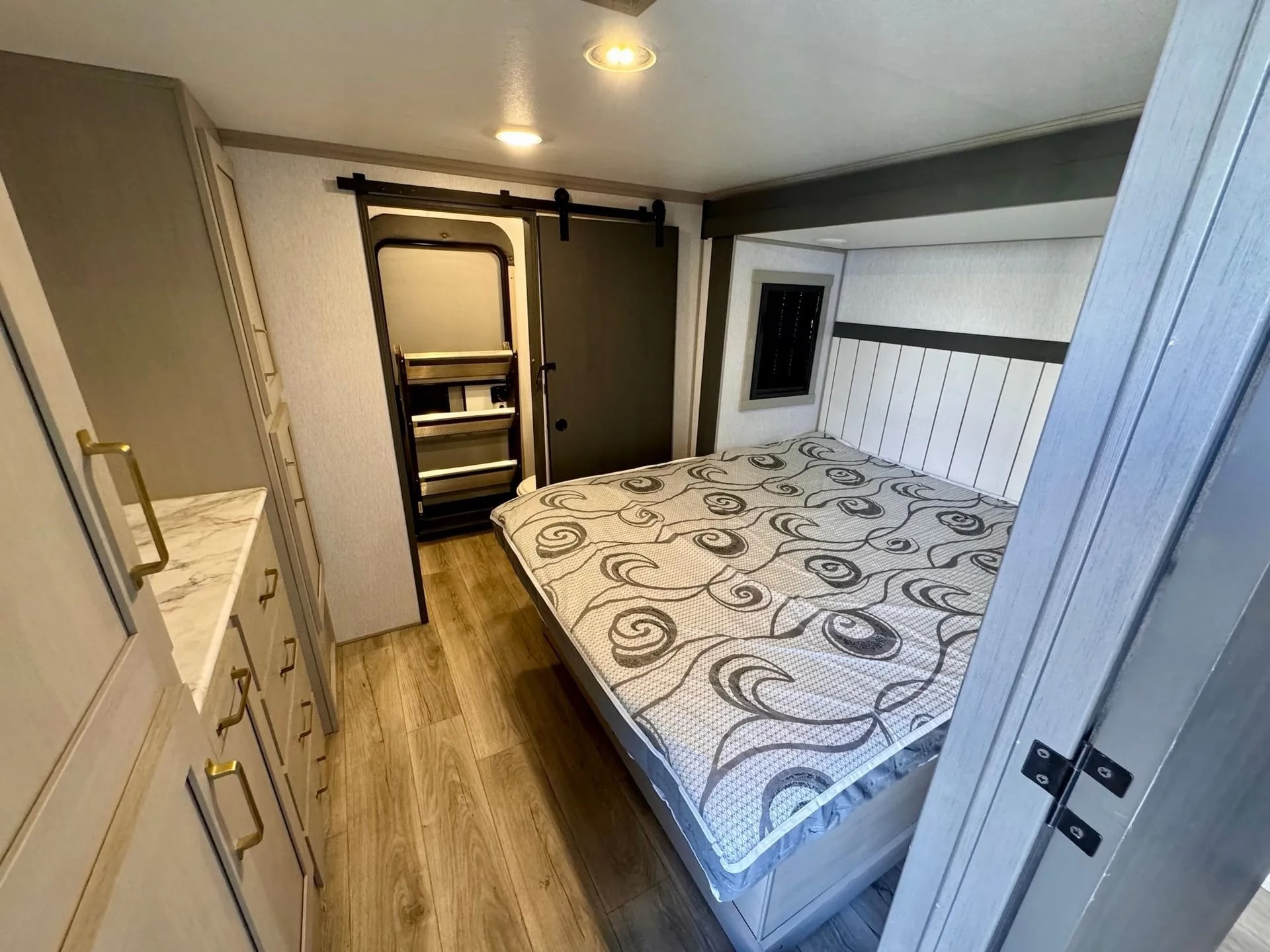 Modern RV rental bedroom featuring a large bed, stylish dresser with gold handles, and sliding barn door closet.. Forest River Wildwood Heritage 2024