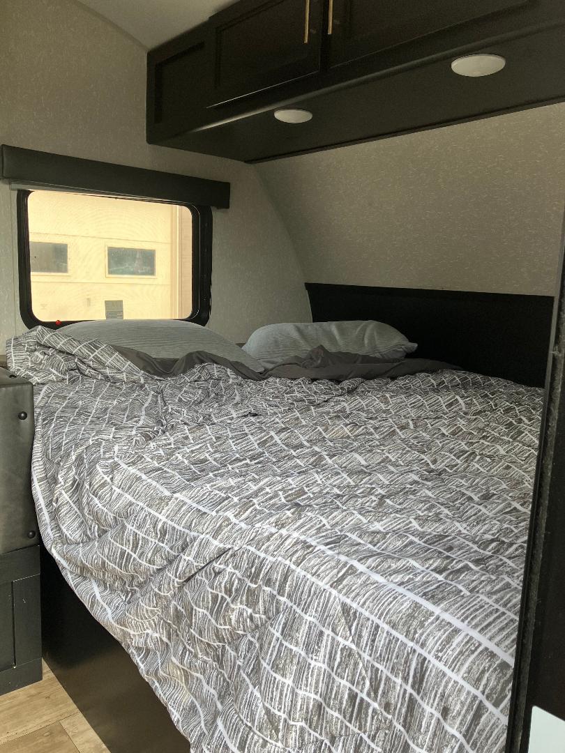 Compact RV rental bedroom featuring a comfy bed with patterned bedding, a window, and overhead storage cabinets.. Forest River Cherokee Wolf Pup 2022