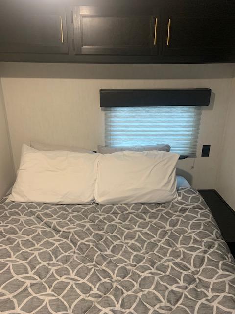 Inside an RV rental: a cozy bedroom features a bed with patterned comforter, dark overhead cabinets, and window blinds.. Forest River Greywolf Black Label 2022
