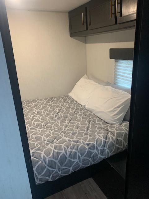 Cozy RV rental bedroom featuring a bed with a gray patterned comforter, white pillow, and dark overhead cabinets.. Forest River Greywolf Black Label 2022