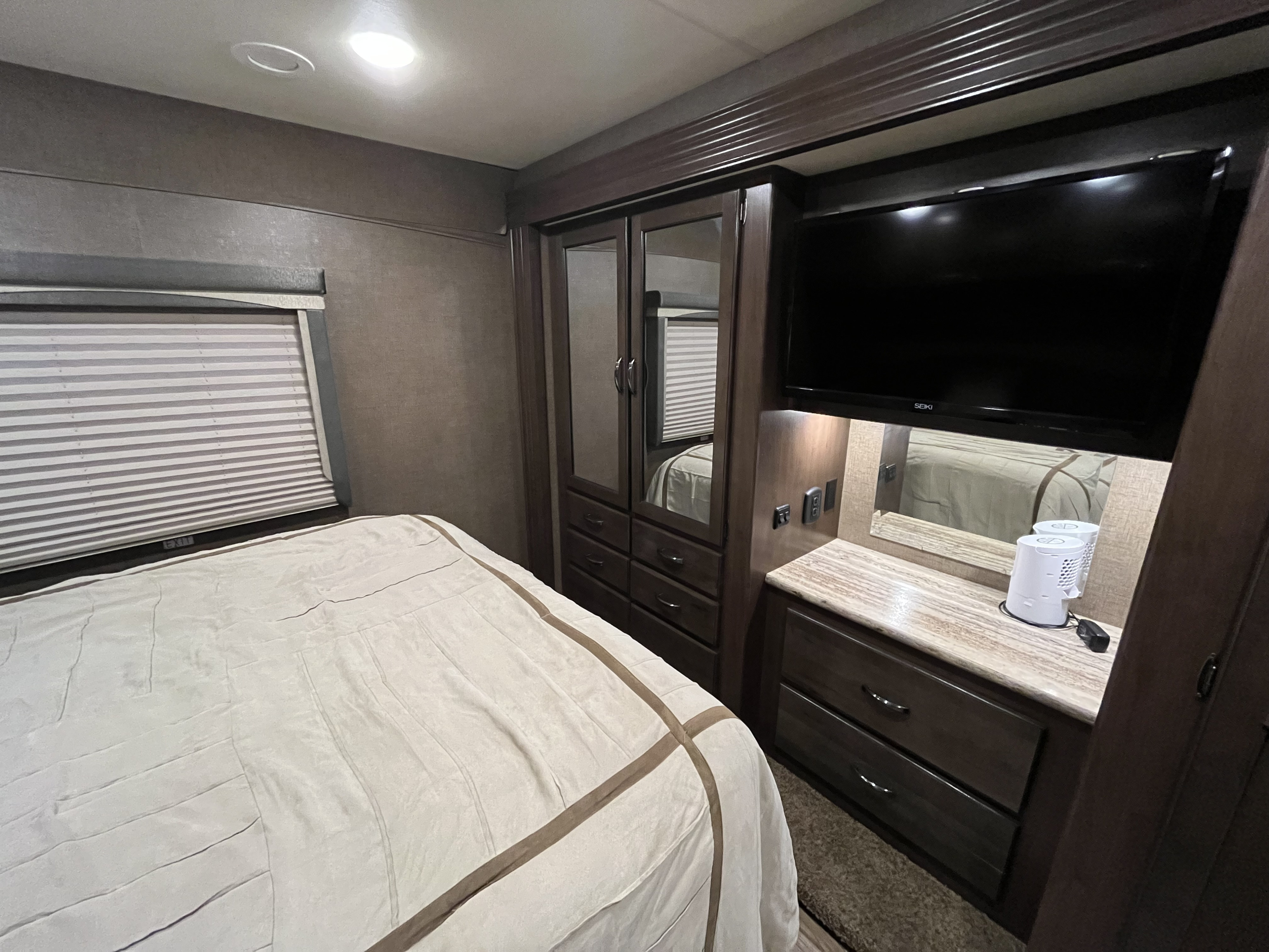Inside an RV rental, a well-appointed bedroom featuring a bed, window blinds, built-in storage, and TV for comfort.. Thor A.C.E. 2016