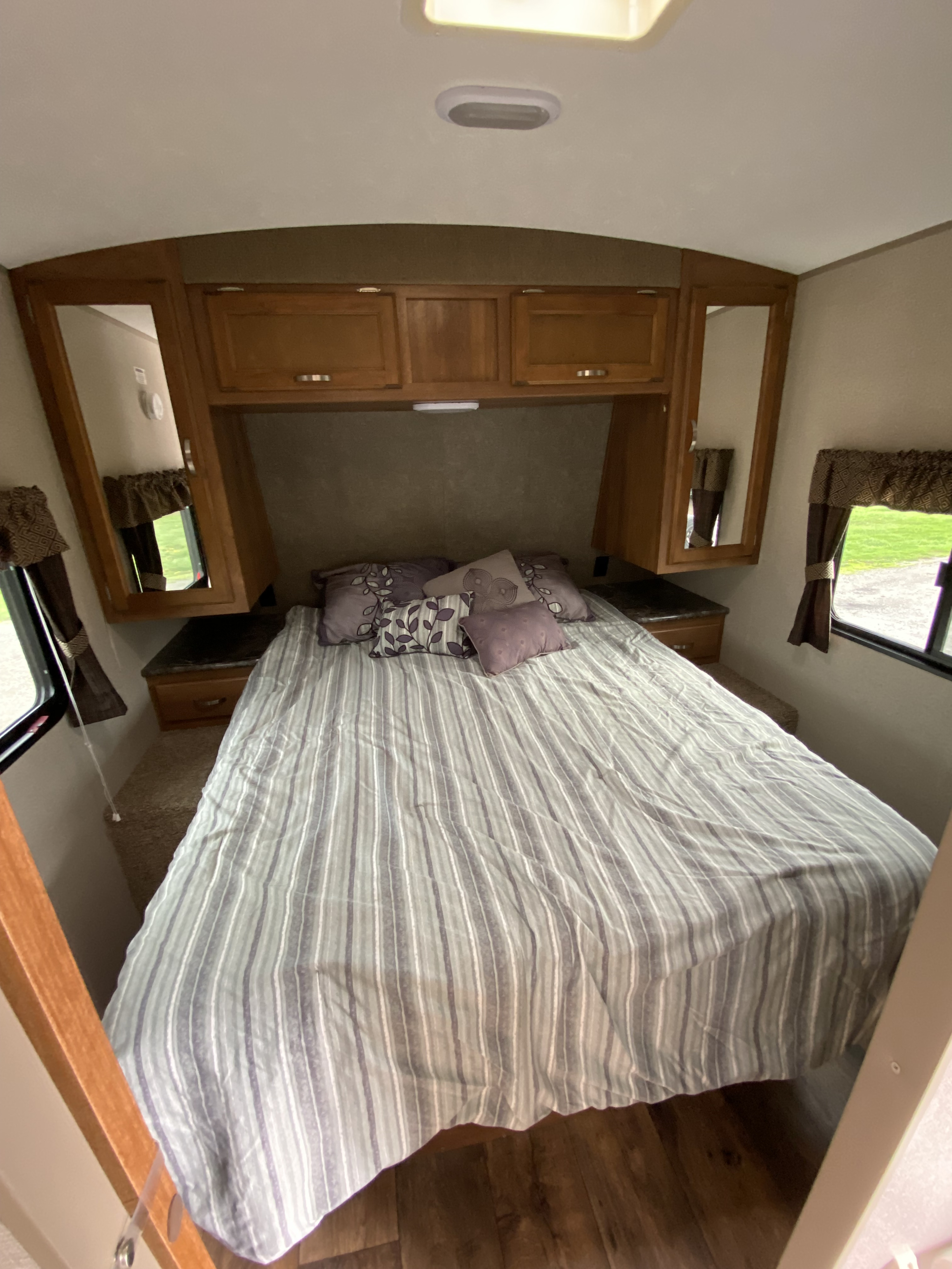 Cozy RV rental bedroom featuring a striped bed, overhead storage, and windows with patterned curtains.. Keystone RV Springdale 2017