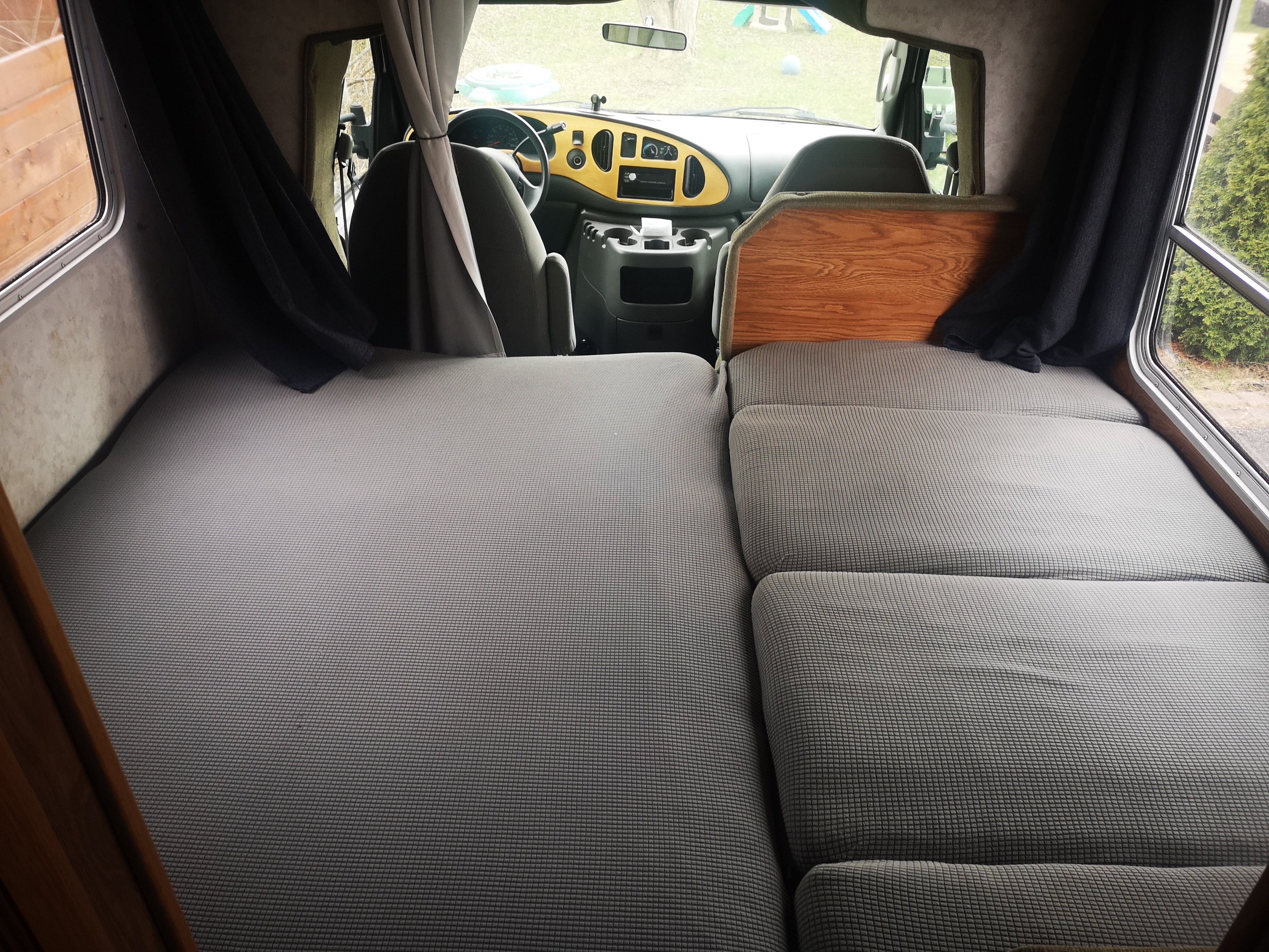 View inside an RV rental showing grey quilted bed/seating, dashboard, and side windows.. Ford F350 2003