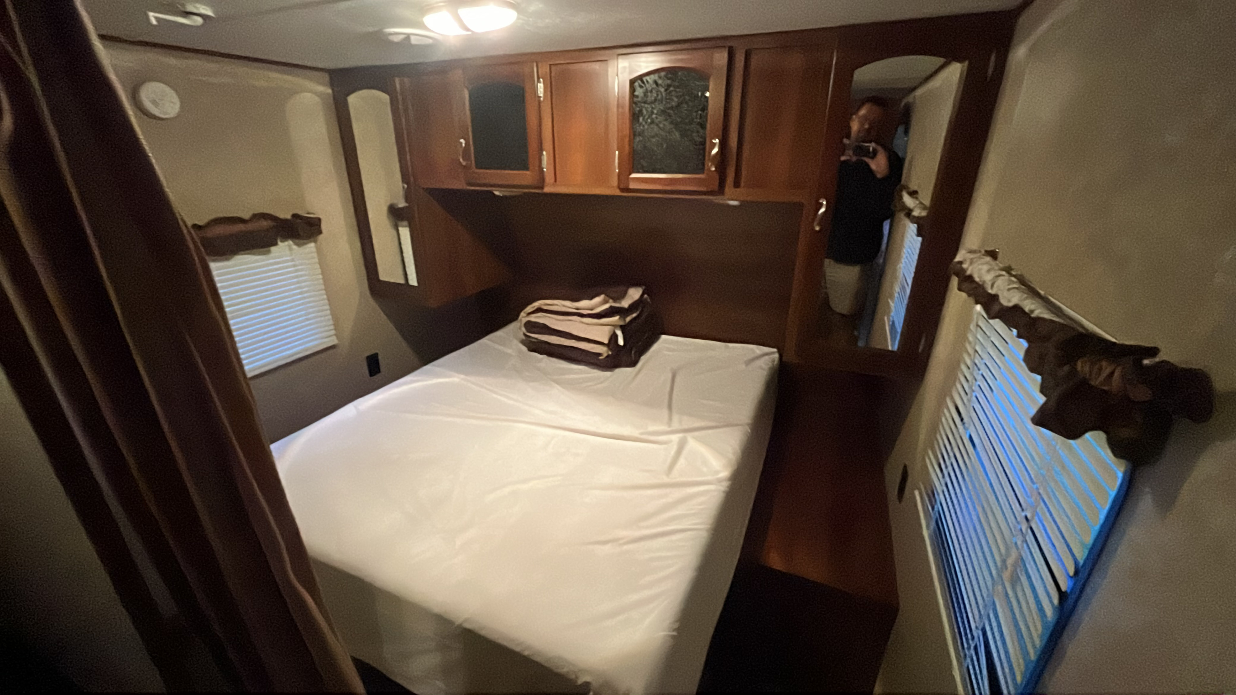 Cozy RV rental bedroom featuring a full bed, overhead cabinets, and windows with blinds.. Forest River Wildwood X-Lite 2023