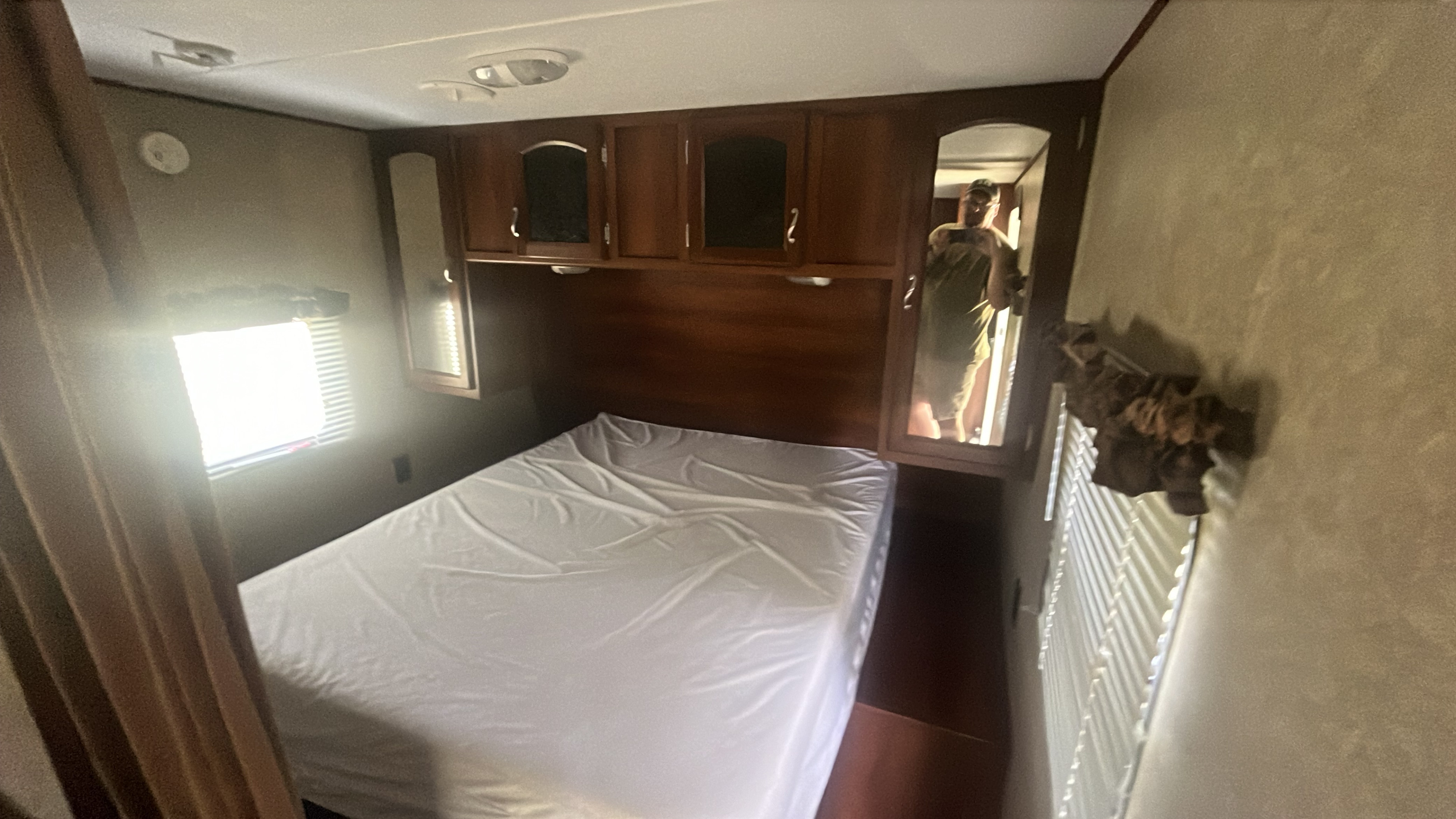 Cozy RV rental bedroom featuring a comfortable bed, ample overhead storage, and natural light from a window.. Forest River Wildwood X-Lite 2023