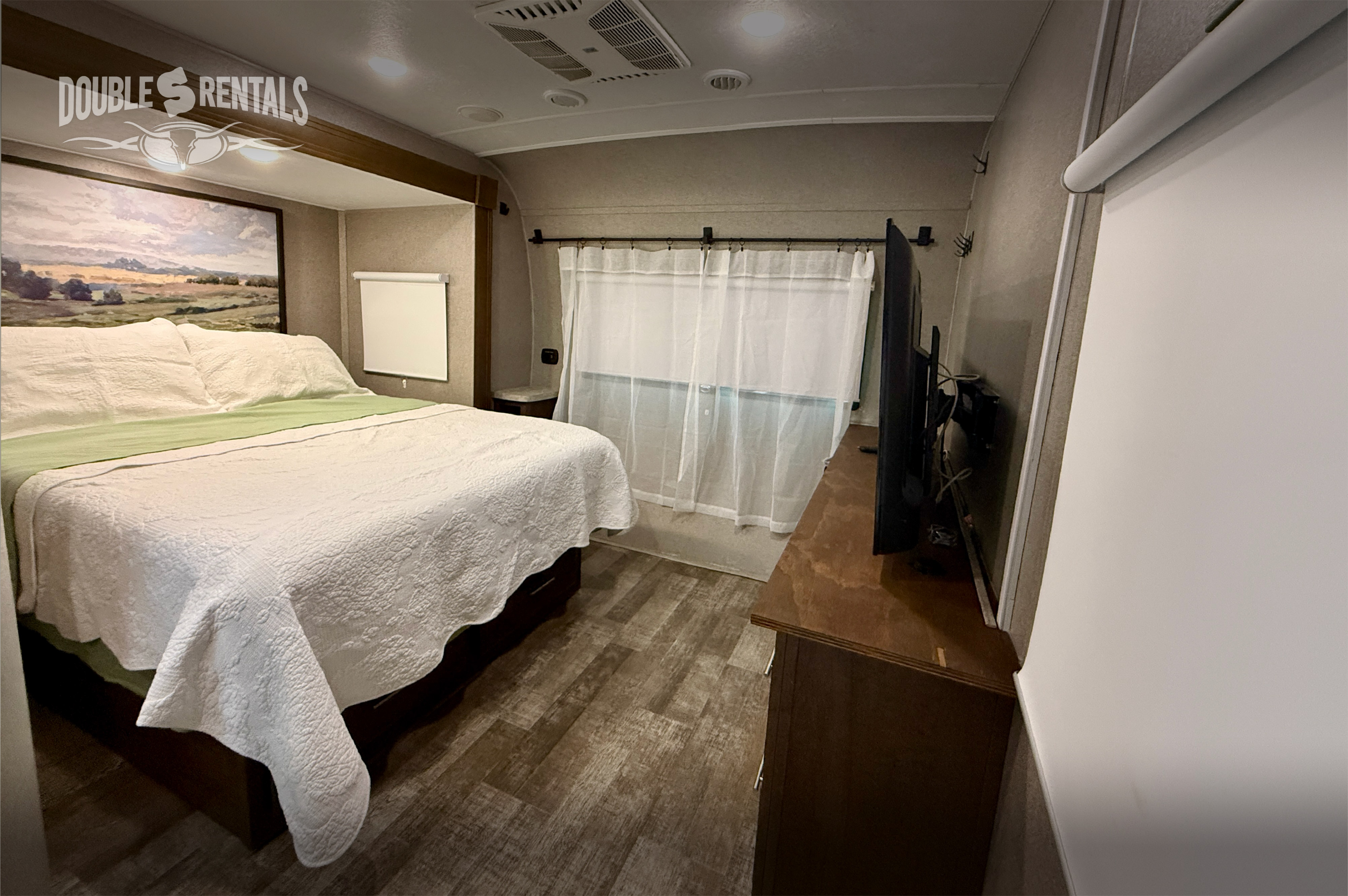 Inviting RV rental bedroom with a large bed, scenic art, flat-screen TV, and practical furnishings for your journey.. Forest River Rockwood Signature 2019