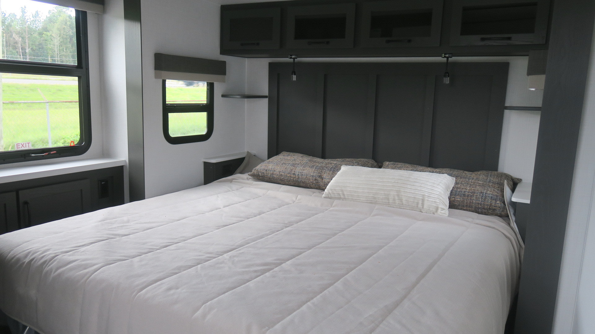 Spacious RV rental bedroom featuring a comfortable bed, dark gray headboard, overhead storage cabinets, and large windows with natural light.. Forest River Rockwood 2025
