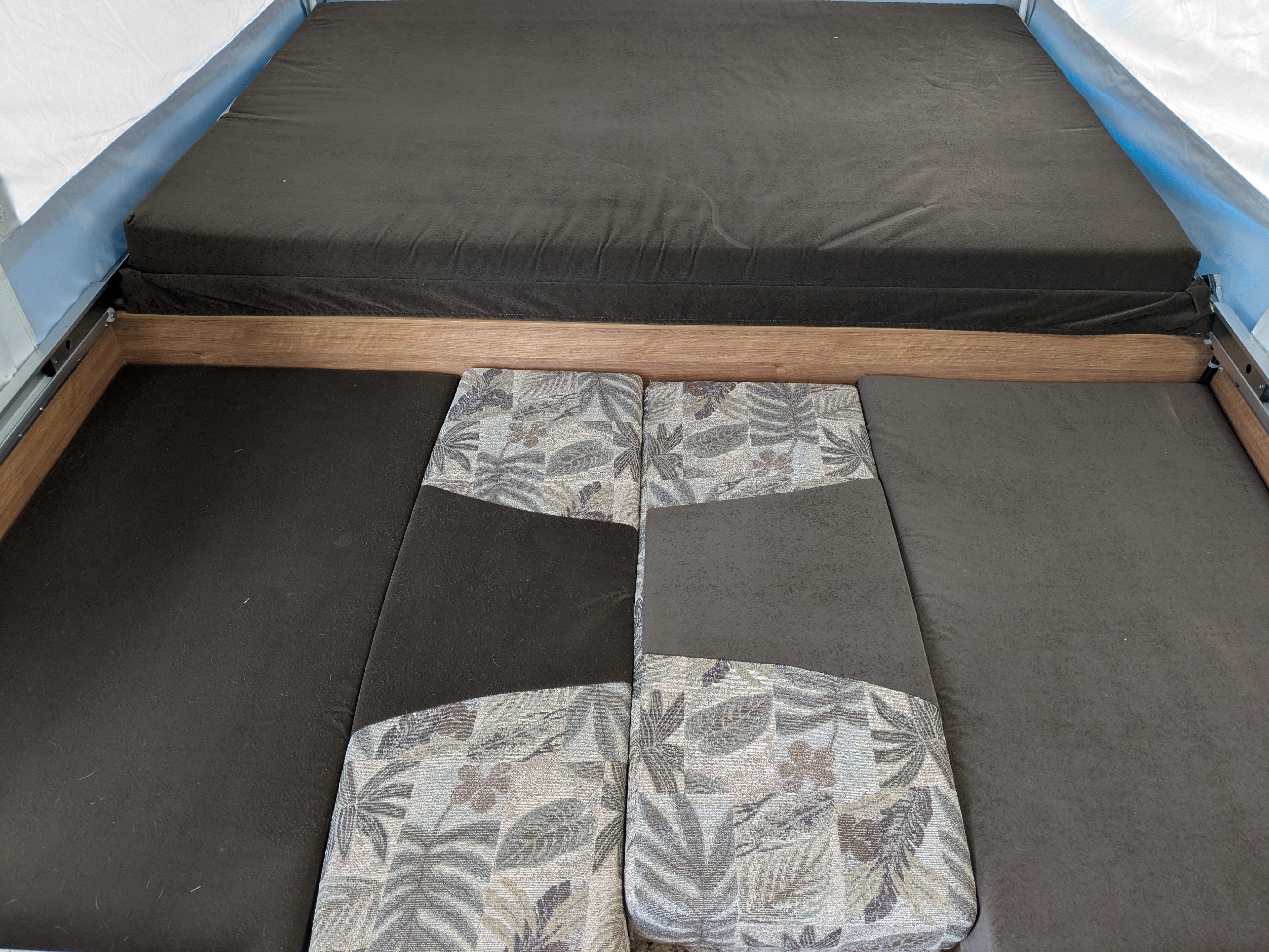 Inside an RV rental: A dark gray bed platform above, with patterned and solid gray cushions forming a seating area below.. Jayco Jay 2010