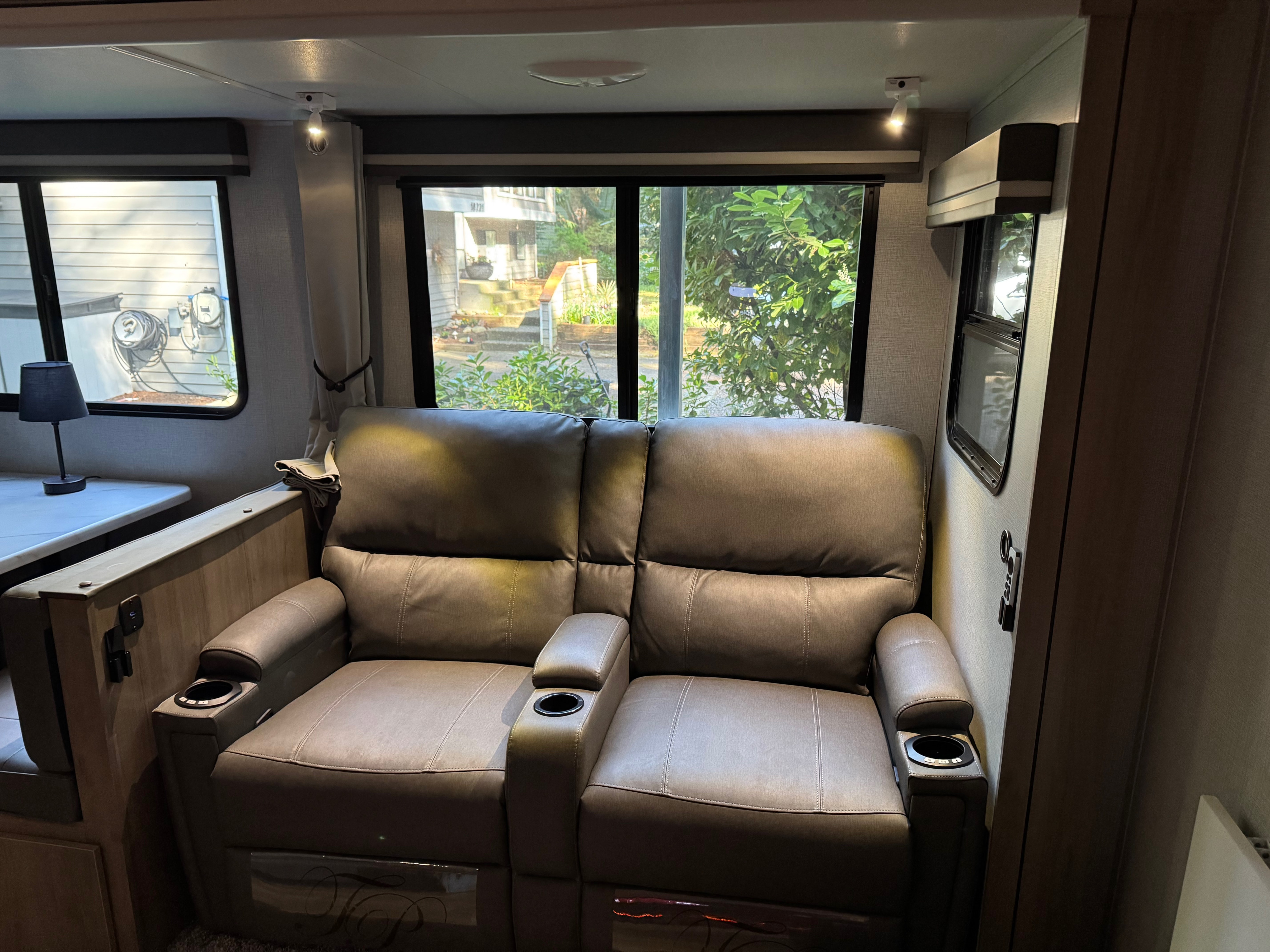 Cozy RV rental interior with plush theater recliners and cupholders, offering comfortable seating with bright window views.. Grand Design Imagine 2023