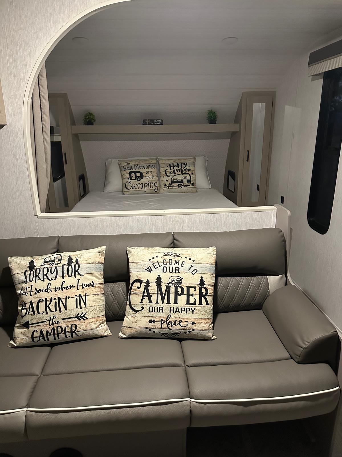 Step into comfort! This RV rental boasts a cozy interior with charming camping-themed pillows on the sofa and bed area.. Forest River Salem Cruise Lite 2023