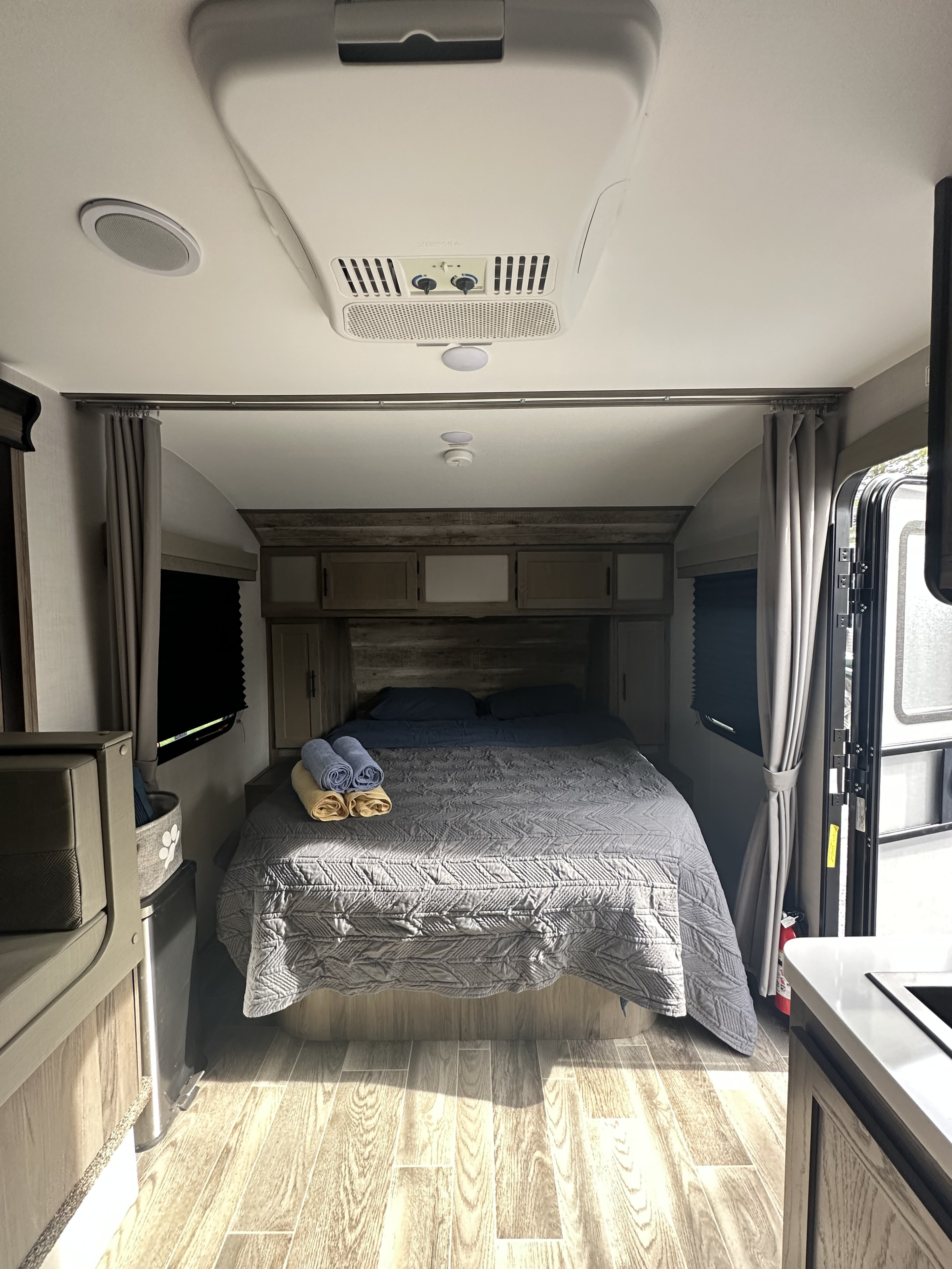 Inside an RV rental: a comfortable bedroom with a large bed, overhead AC, storage, and wood-look flooring.. Gulf Stream Geo 21 QBS 2023