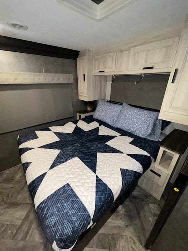 Spacious RV rental bedroom featuring a blue star quilt, ample storage cabinets, and an upper bunk.. Forest River Sunseeker 2022