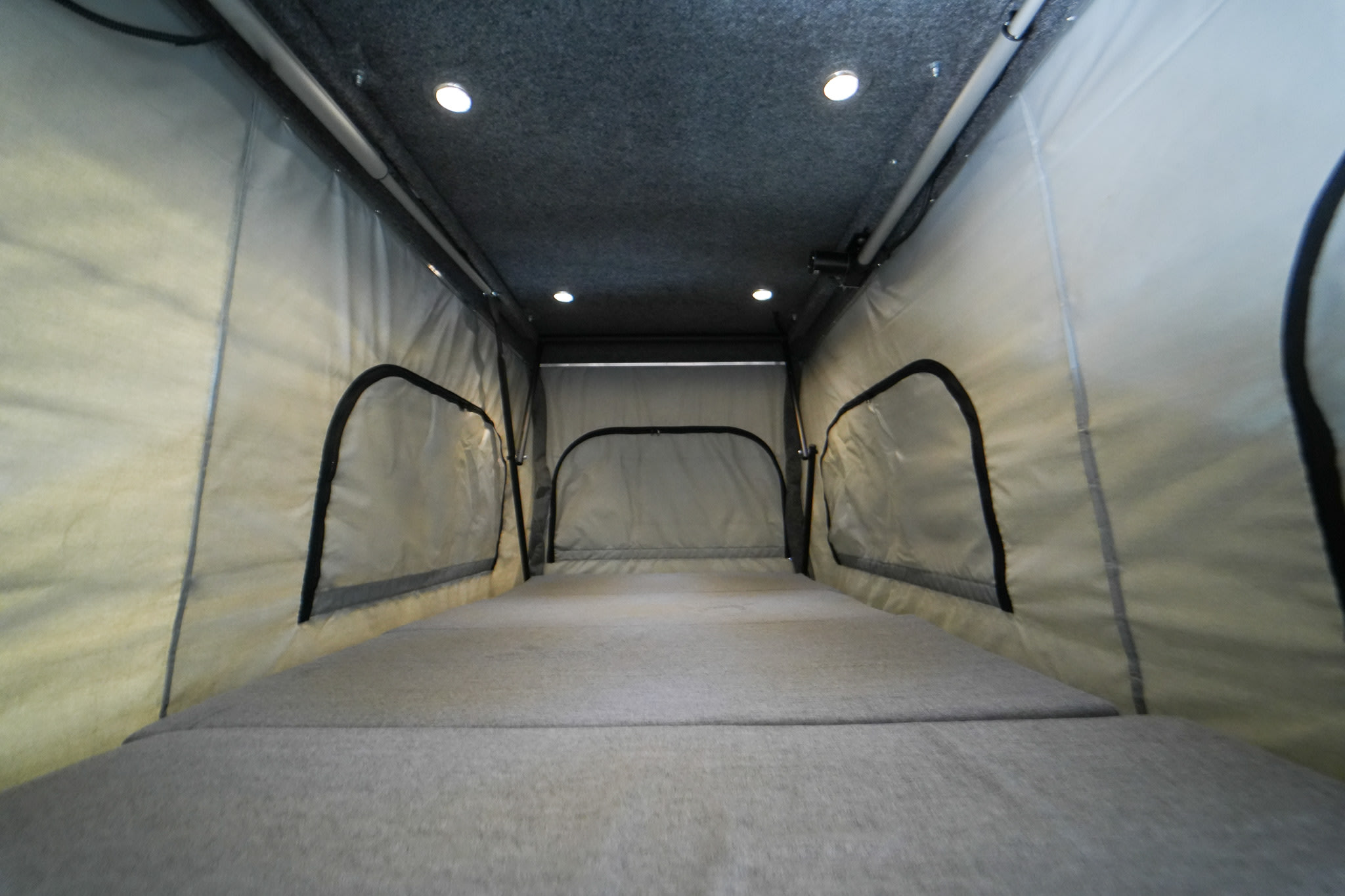 Pop-top sleeping area of an RV rental with comfortable gray mattress, fabric walls, arched windows, and bright lighting.. Mercedes-Benz Sprinter 2021