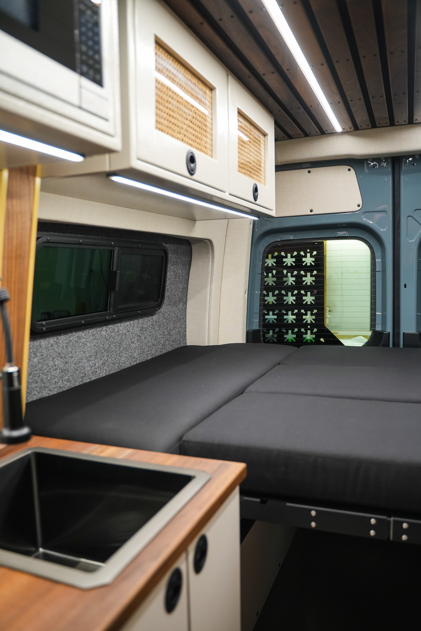 Spacious rv rental camper van interior featuring a comfy bed, kitchen sink, and clever overhead storage.. Mercedes-Benz Sprinter 2021