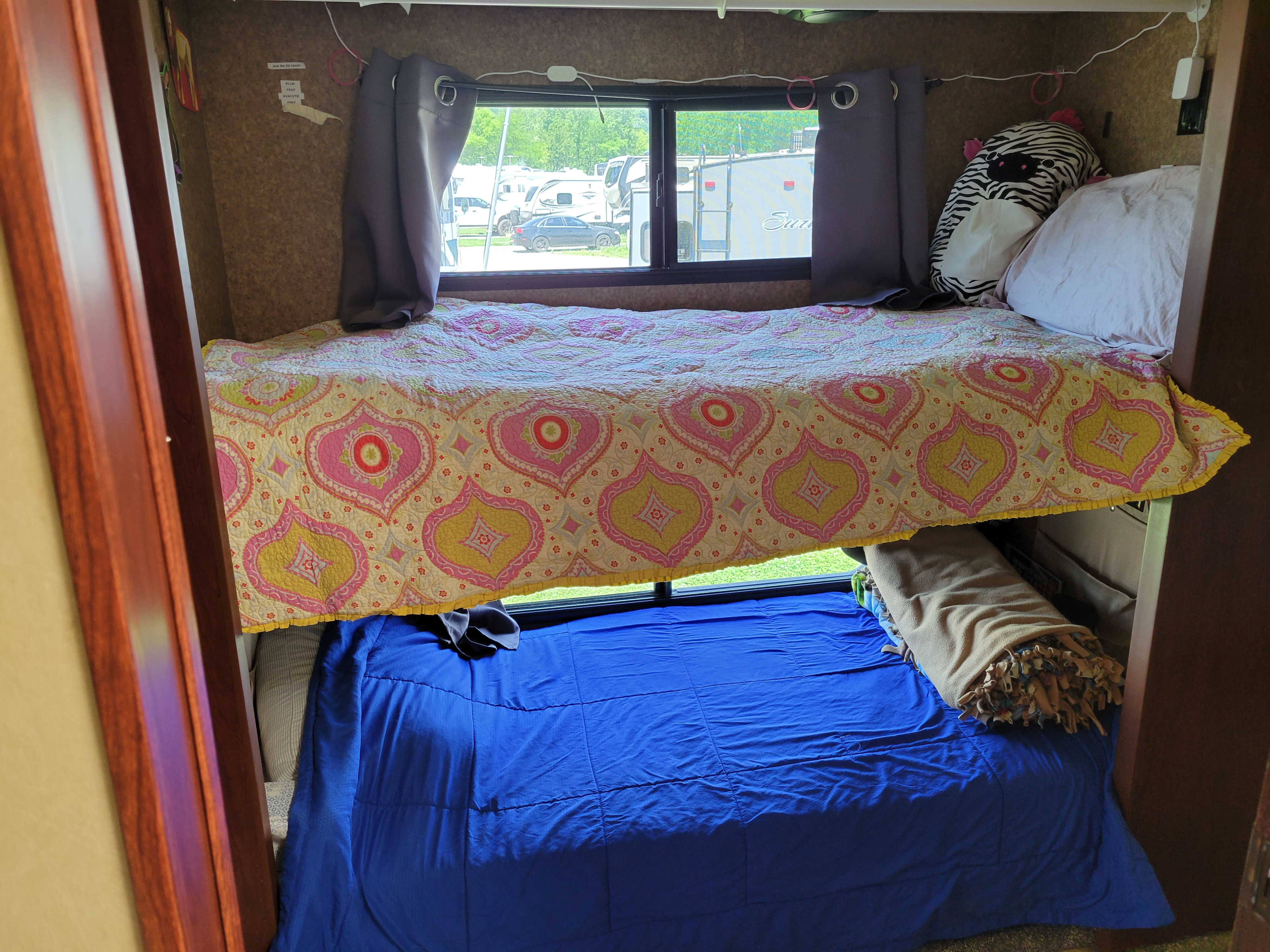 Cozy RV rental bunk beds with a colorful quilt and blue comforter. Window offers a view of the campsite.. Forest River Berkshire 390-Bunkhouse 2012
