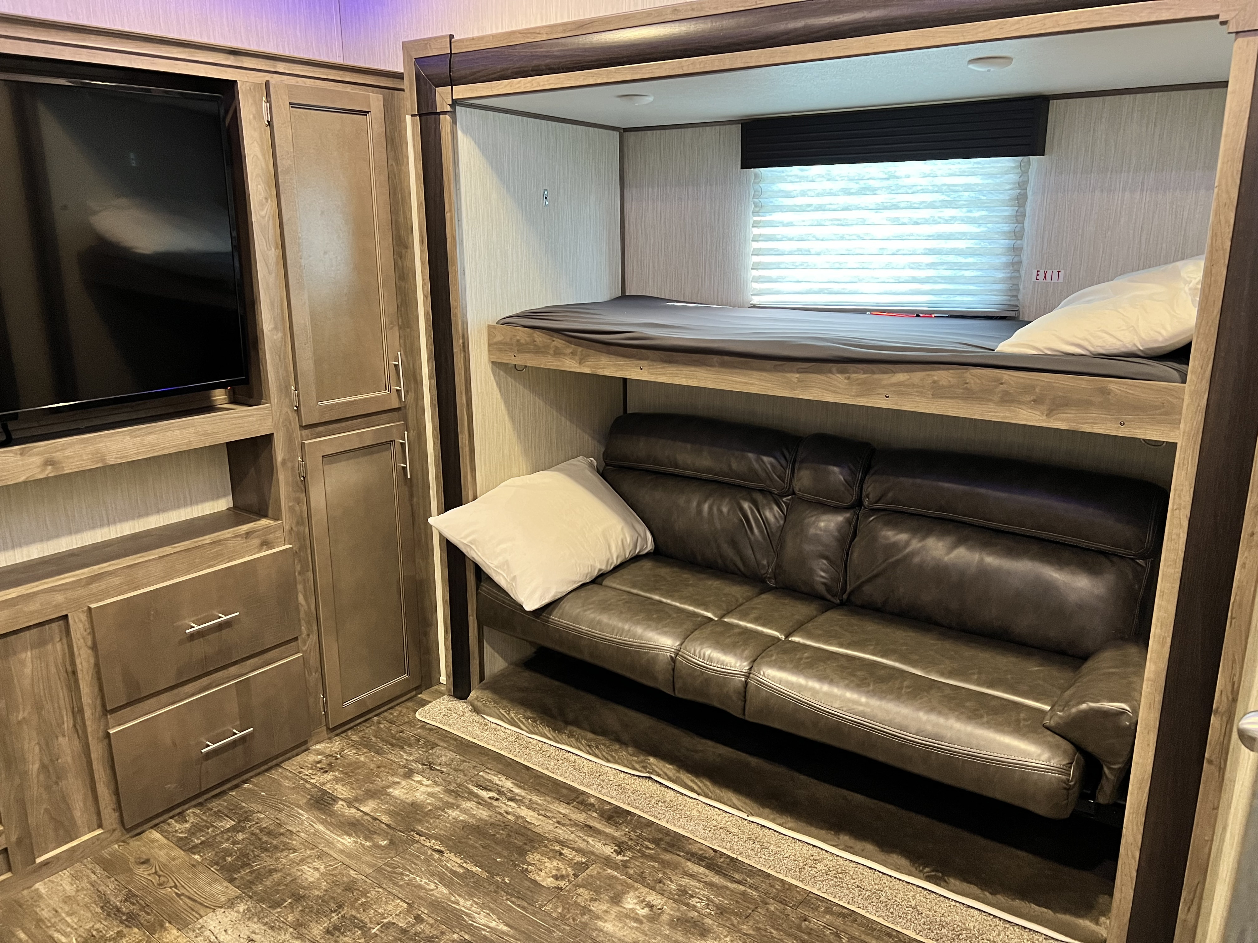 Inside an RV rental: a bunk bed above a leather sofa, with a TV & cabinetry on the left. Ideal for compact living.. Forest River Sabre 2019