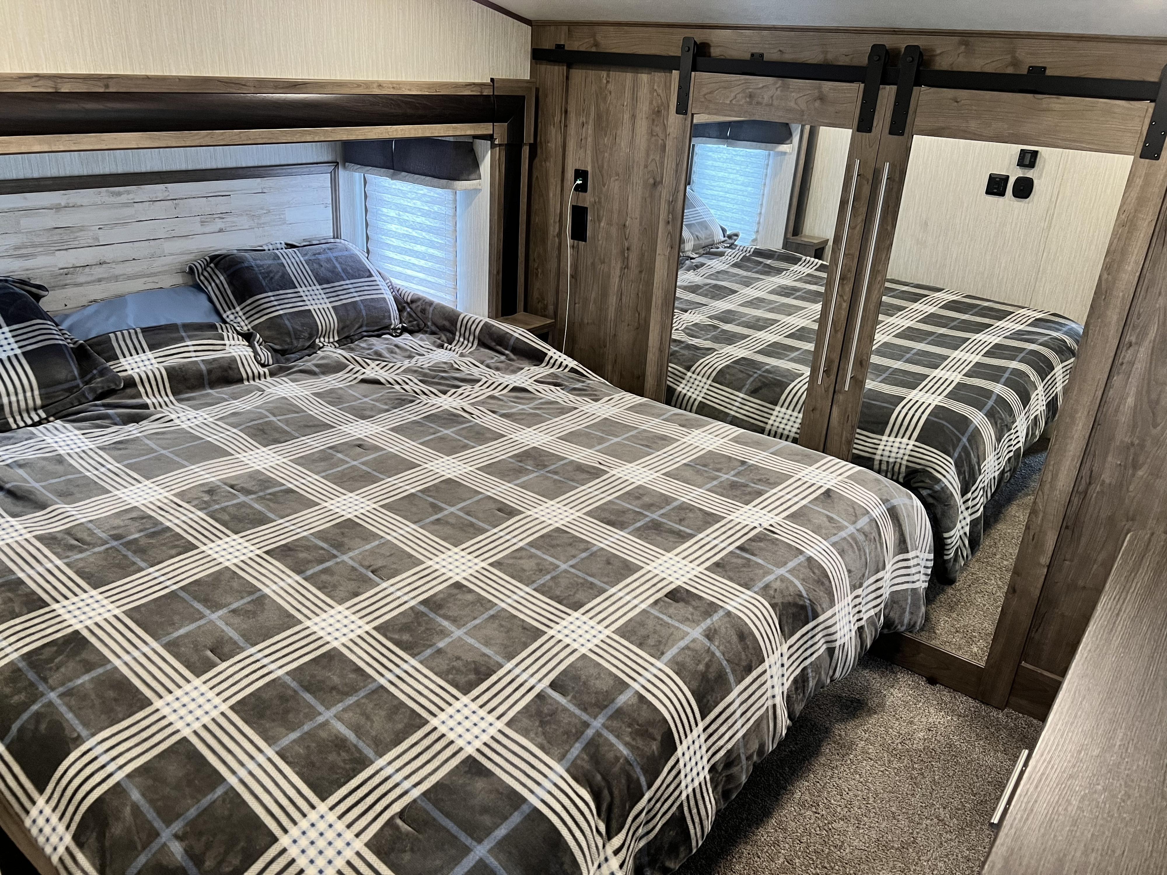 Cozy RV rental bedroom with plaid bedding, a rustic headboard, and mirrored sliding closet doors, reflecting the bed.. Forest River Sabre 2019