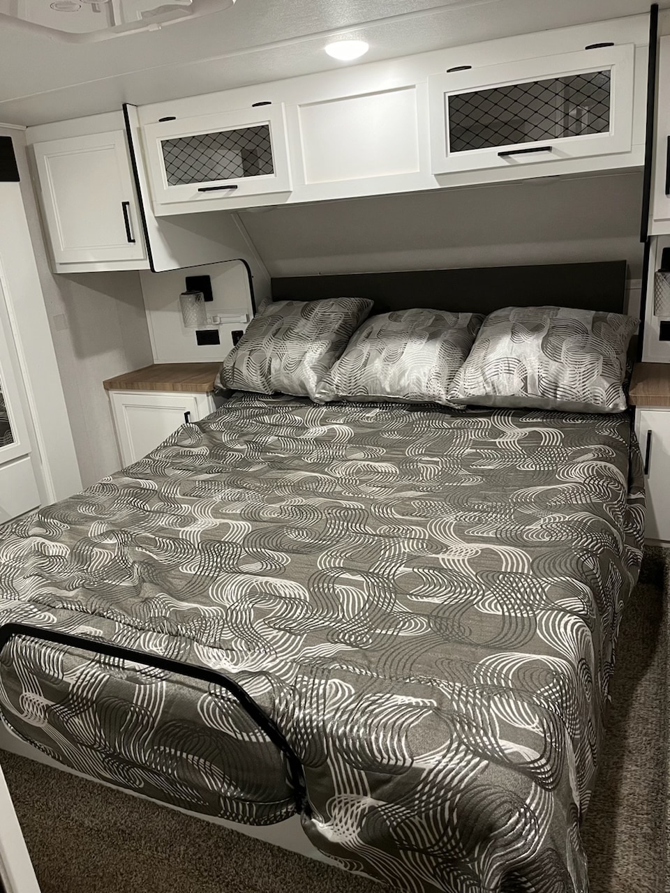 Cozy RV rental bedroom features a patterned bed, built-in nightstands, and white overhead cabinets with mesh accents.. Crusader Lite 2021
