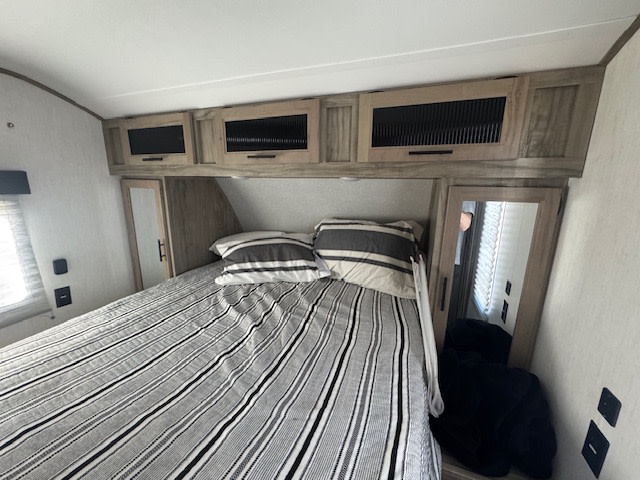 RV rental bedroom with striped bed, overhead cabinets, and mirrored side storage, optimizing a compact space.. Forest River Cherokee Alpha Wolf 2021