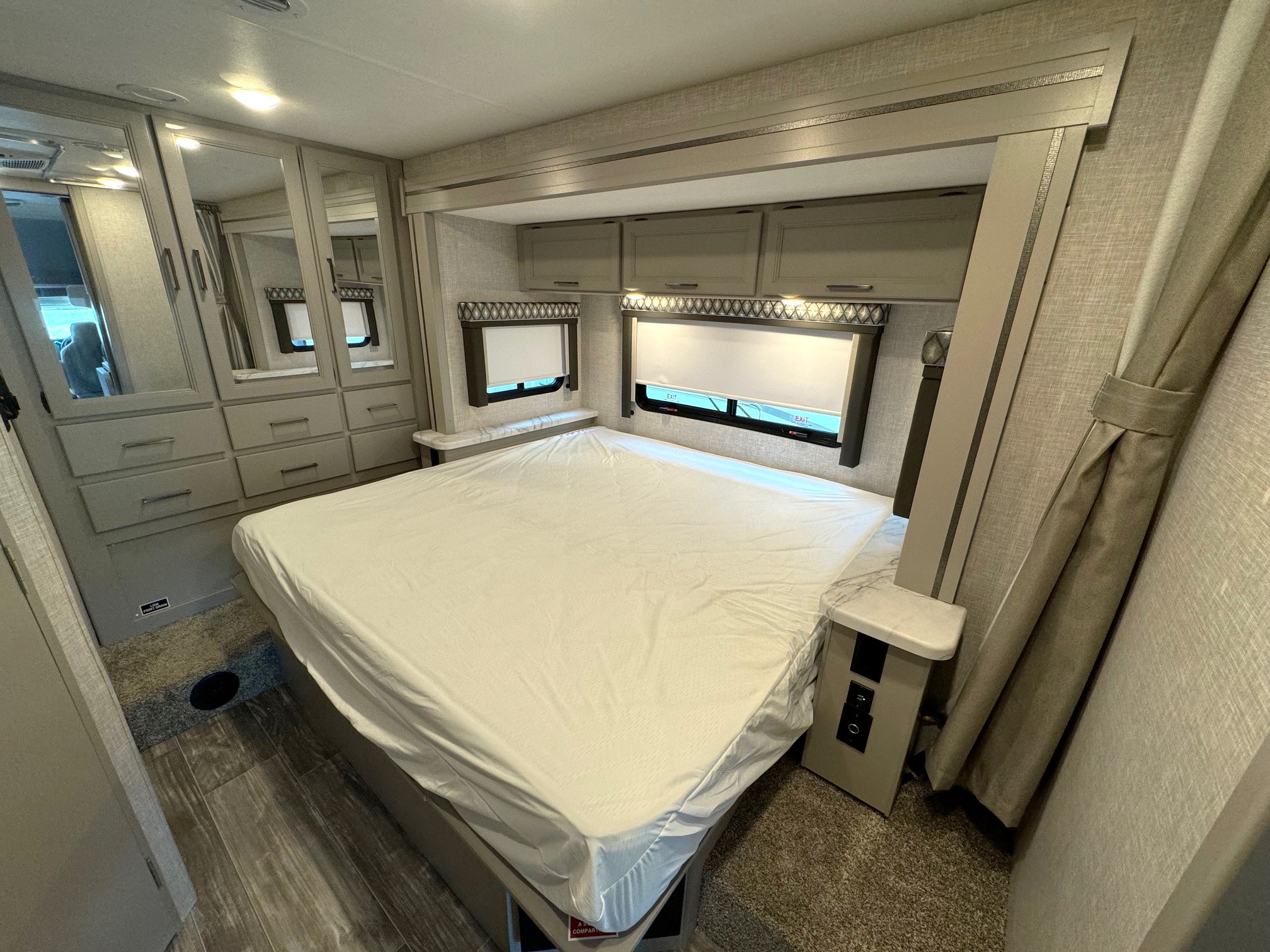 RV rental bedroom with a comfortable bed, mirrored closets, overhead cabinets, and windows.. Thor Motor Coach Geneva 2025